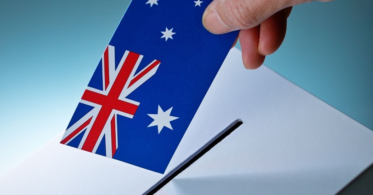 Hand dropping an Australian flag-themed ballot into a ballot box, symbolizing voting.