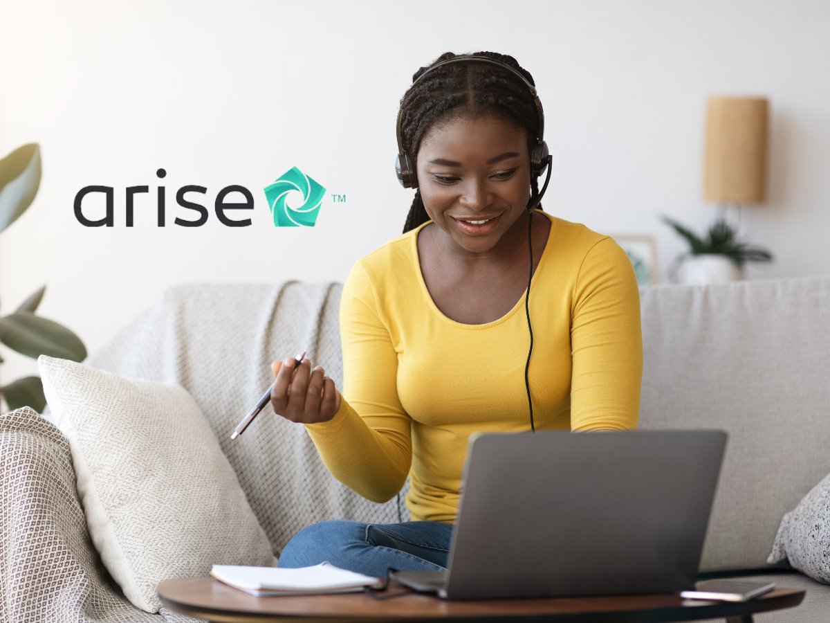 A person wearing a headset works on a laptop while sitting on a sofa next to an Arise logo.