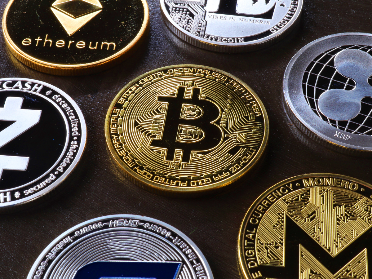 A variety of physical cryptocurrency coins including Bitcoin, Ethereum, and Ripple on a dark surface.