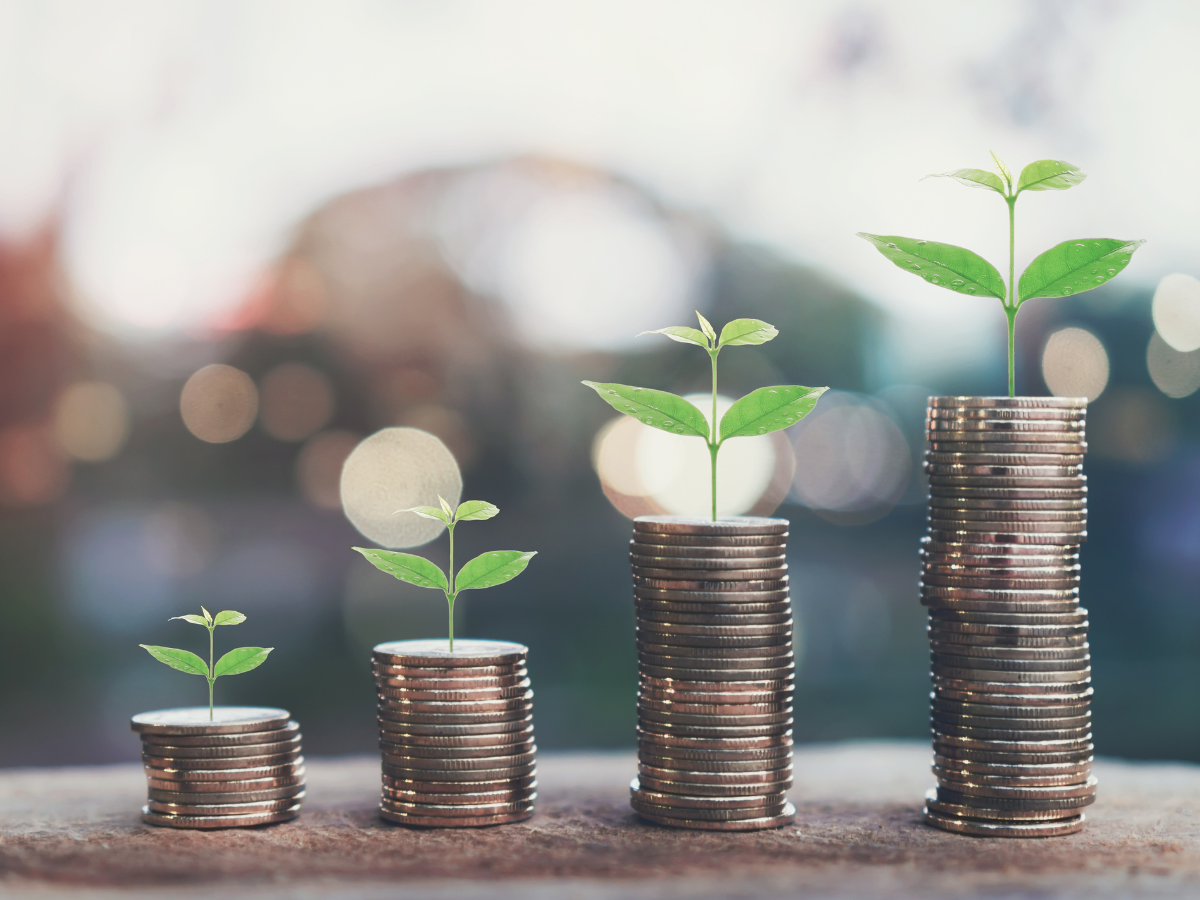 Four stacks of coins of increasing height, each topped with a small green plant, symbolizing financial growth.