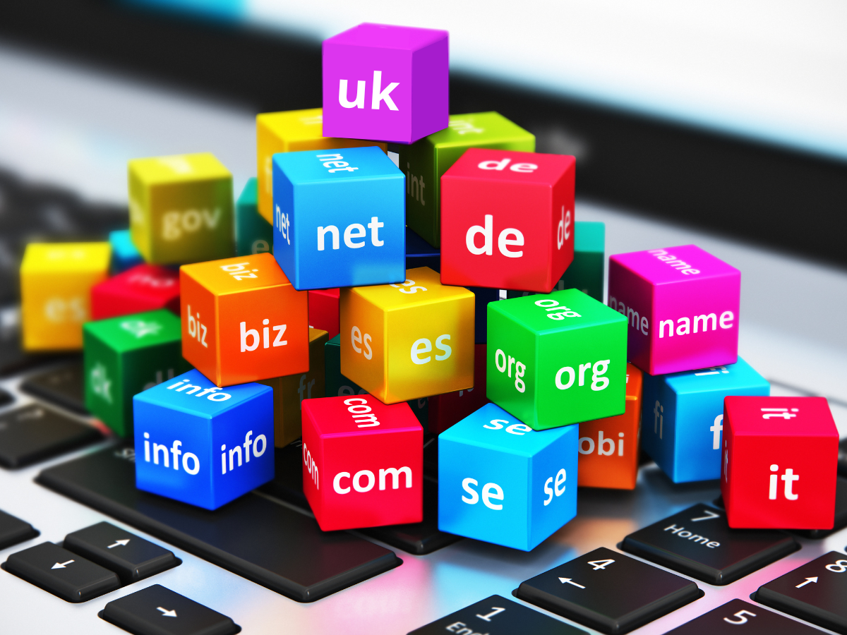 Colorful blocks with various top-level domain extensions like .com, .net, and .org resting on a laptop keyboard.