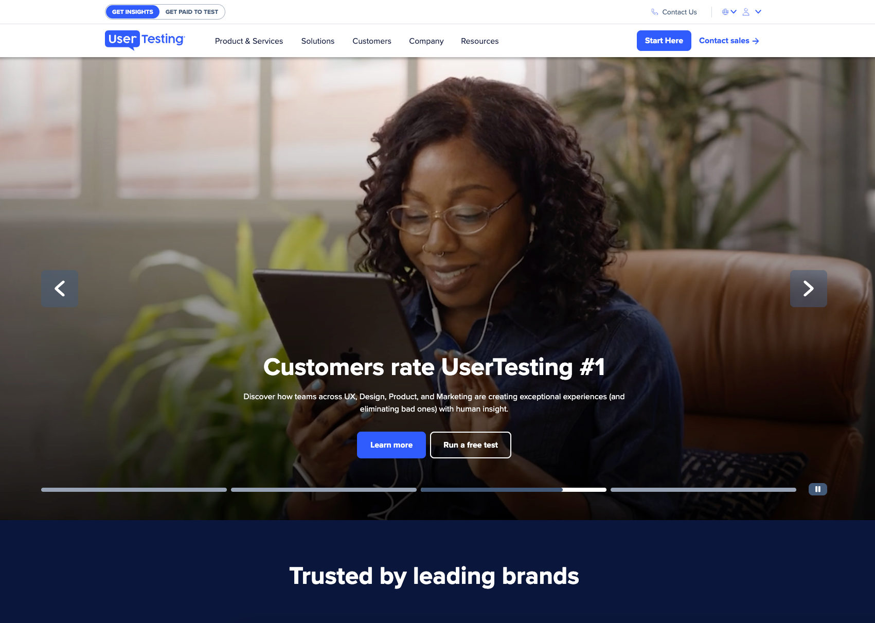 A person wearing glasses and earphones holds a tablet while viewing a UserTesting website hero banner.