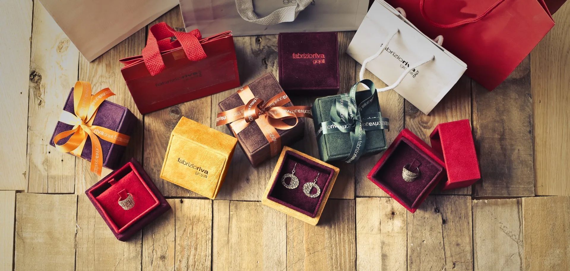A collection of gift boxes, shopping bags, and open jewelry boxes with earrings and rings displayed on a wooden surface.