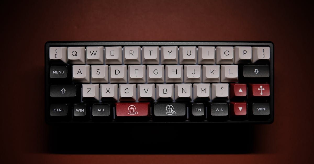 A compact mechanical keyboard with custom light, black, and red keycaps, positioned on a dark red surface.