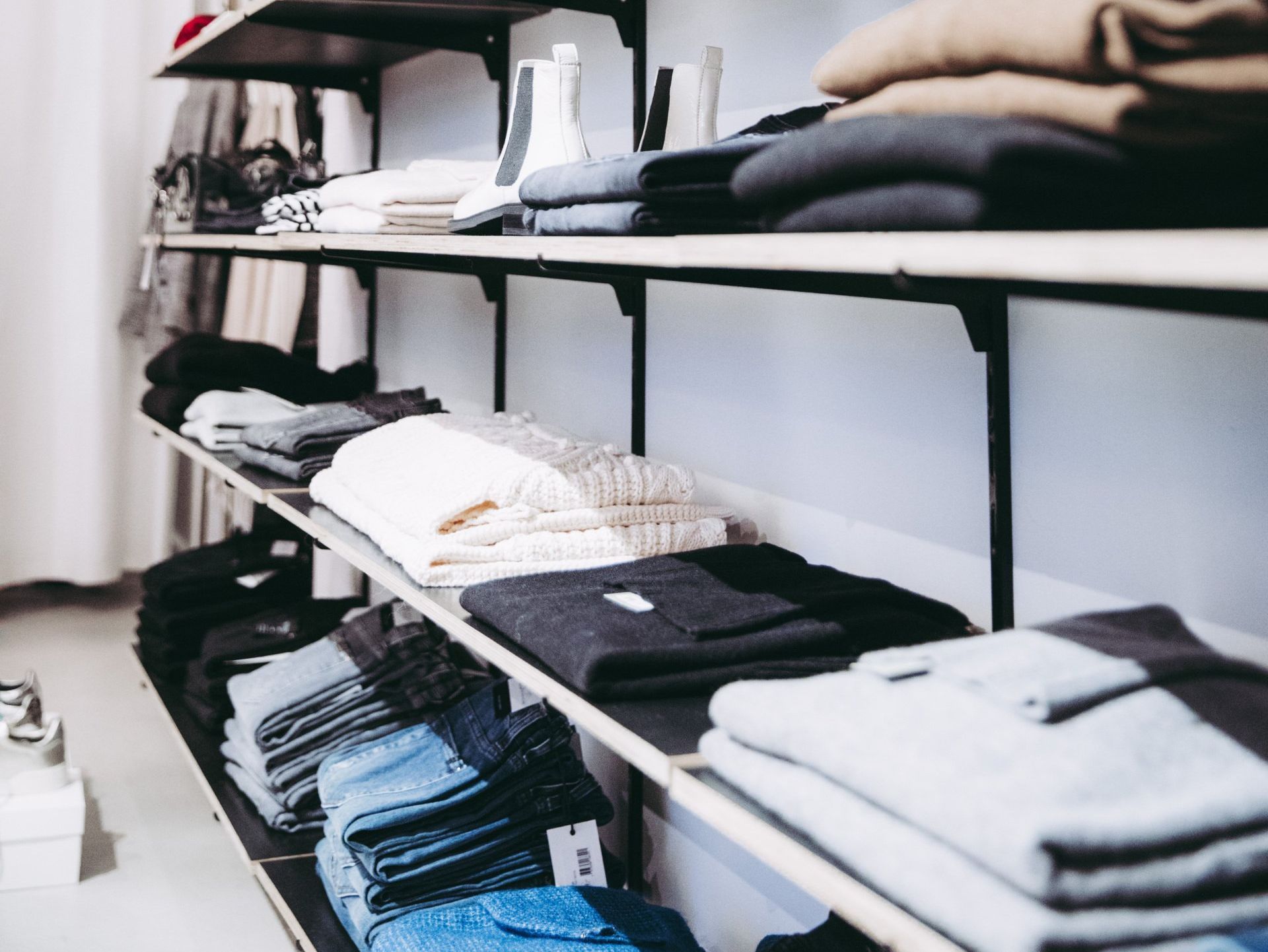 Shelves in a retail store displaying folded sweaters and denim jeans in neutral colors.
