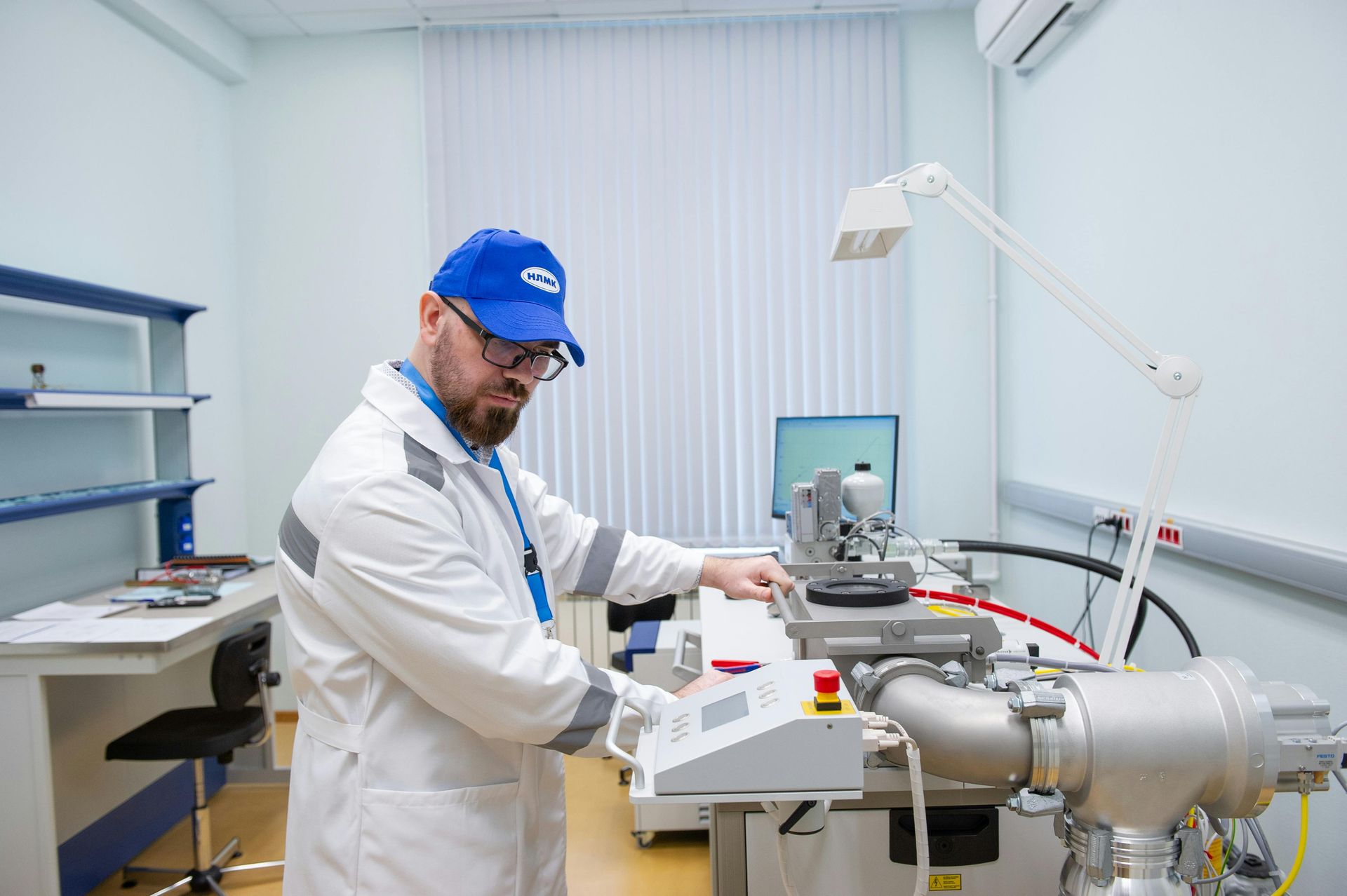 Technician in lab coat and blue cap operating industrial equipment in a sterile laboratory.