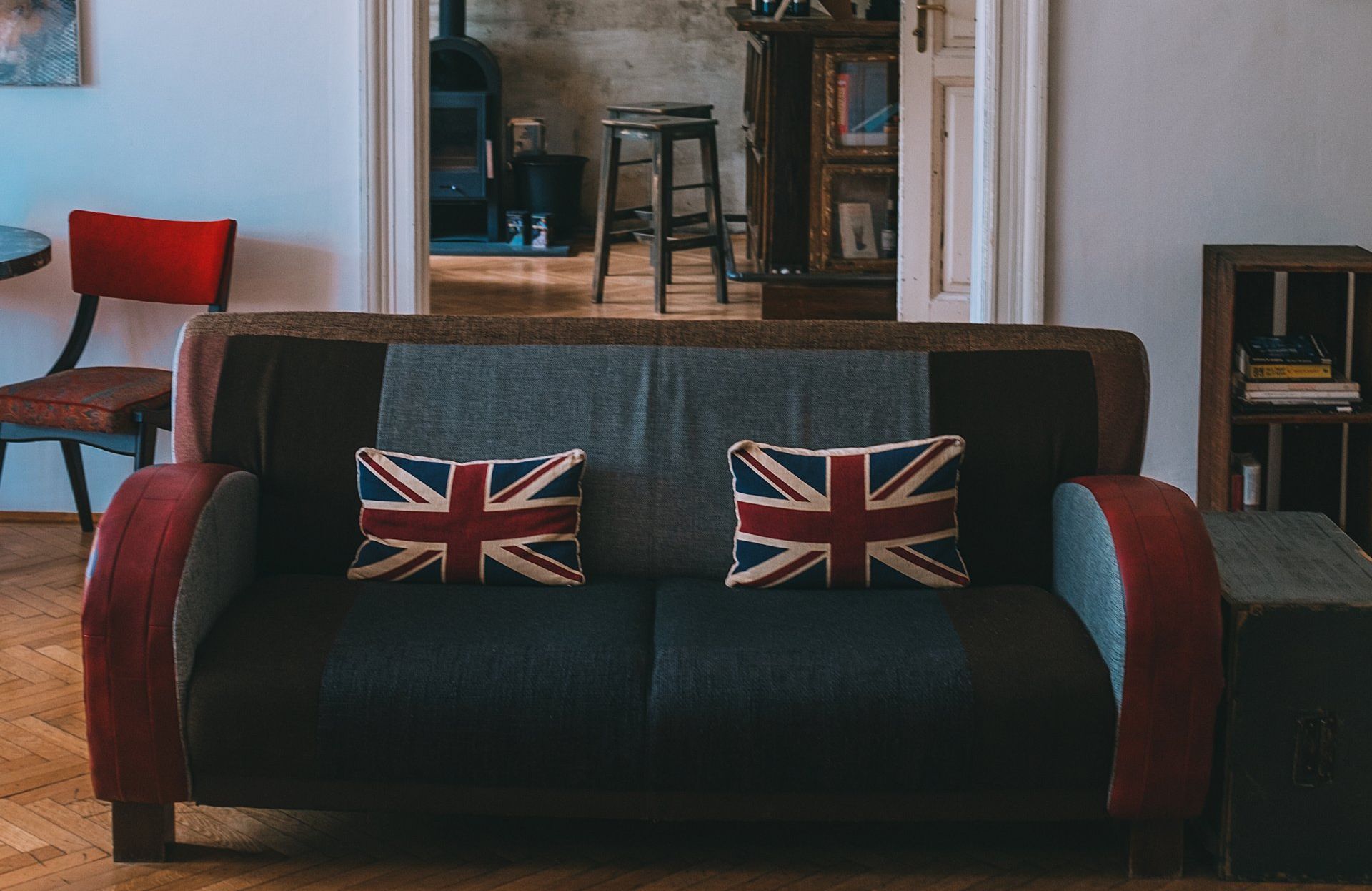 A dark gray sofa with two Union Jack pillows in a room with a red chair and a wooden stool visible in the background.