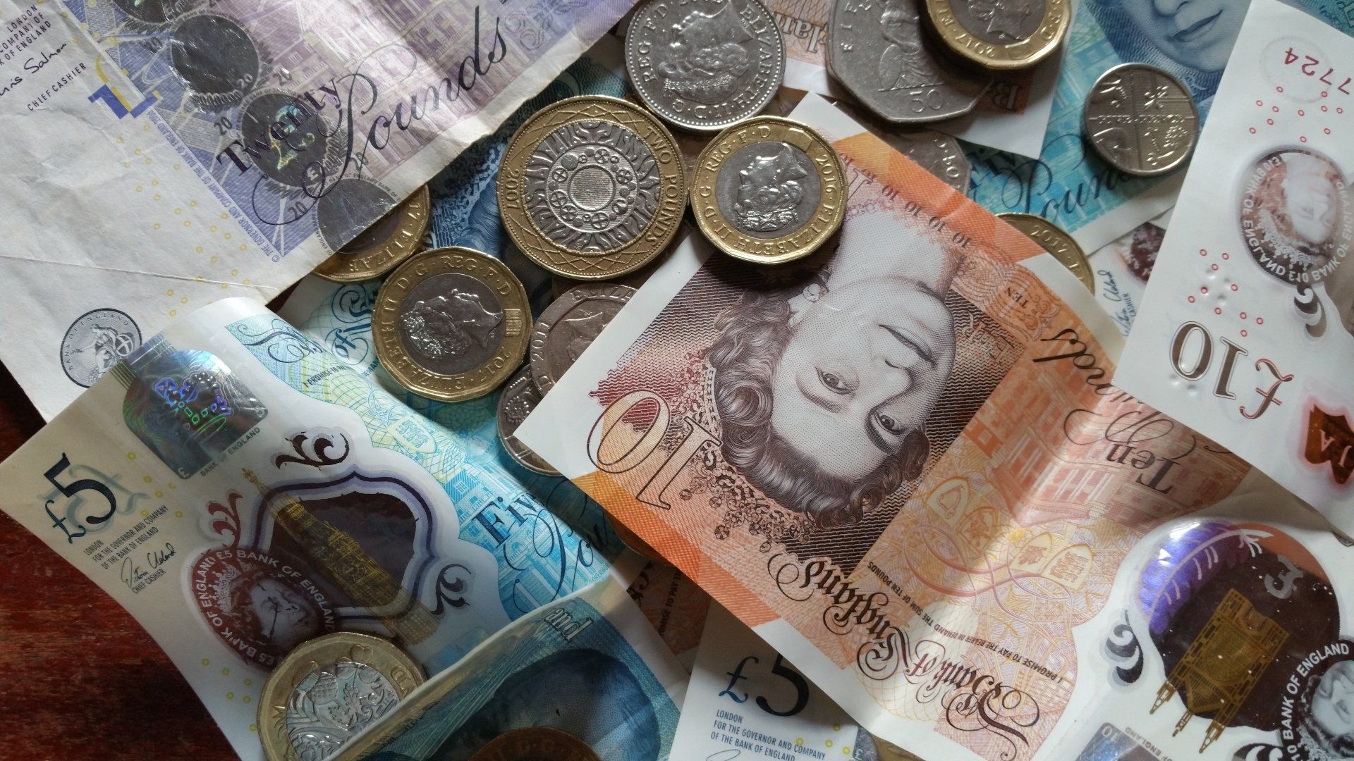 A scattering of British pound banknotes and coins of various denominations on a dark surface.
