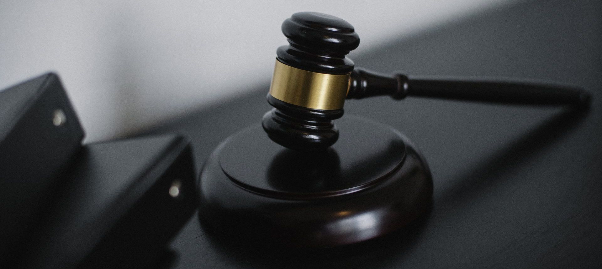 A wooden gavel with a brass band rests on a matching sounding block next to a black document binder.