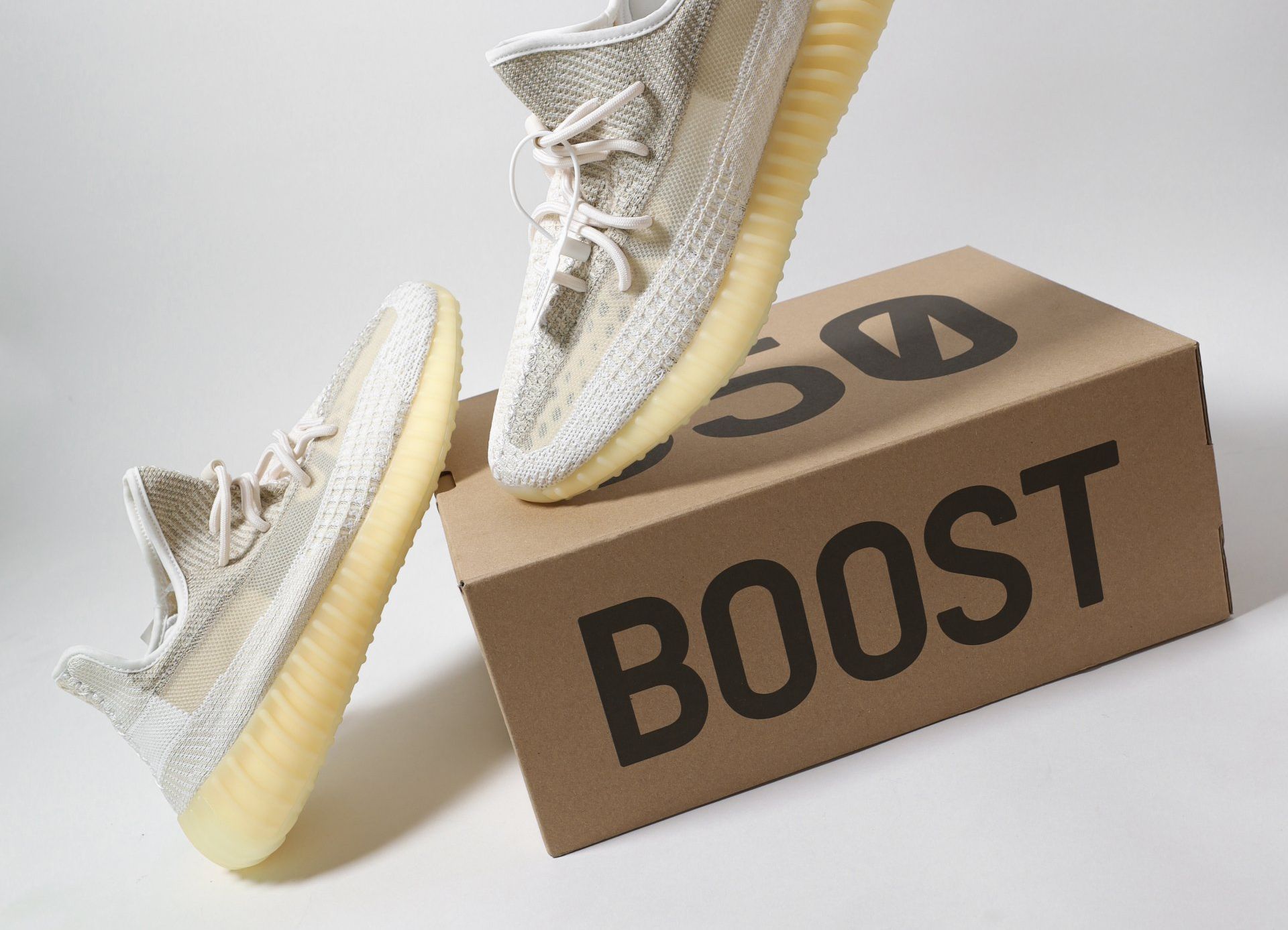 A pair of light-colored Yeezy 350 sneakers floating above a brown cardboard box labeled 