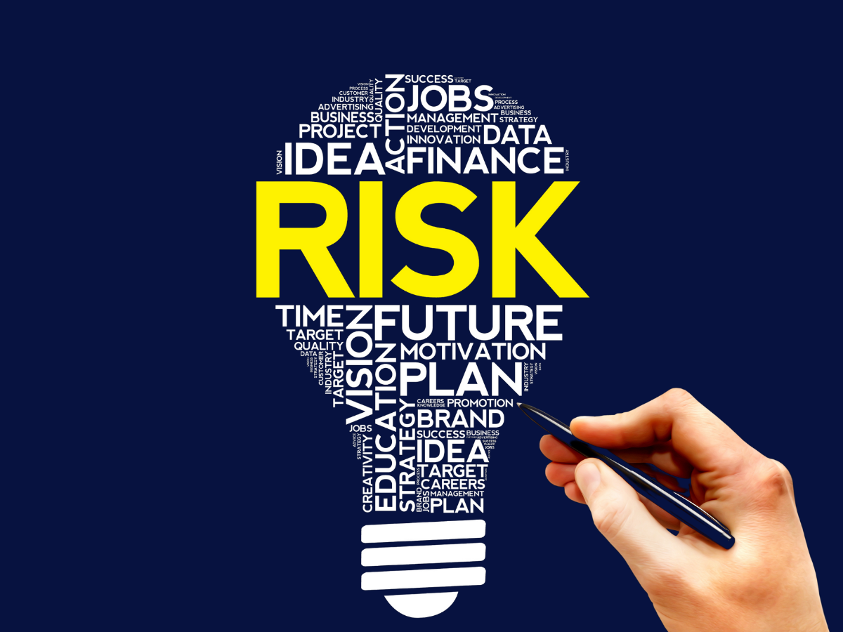 A hand holds a pen near a lightbulb silhouette filled with business-related words, with the word 
