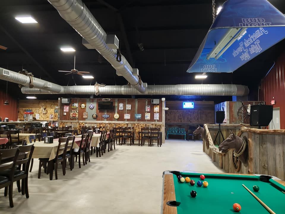 A rustic event space with dining tables, a pool table in the foreground, and exposed industrial ductwork on the ceiling.