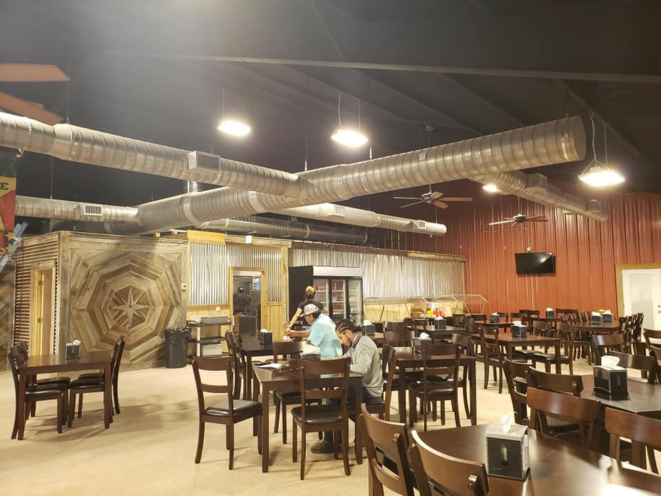 An indoor dining area with tables and chairs, industrial-style exposed ductwork on the ceiling, and rustic wall decor.