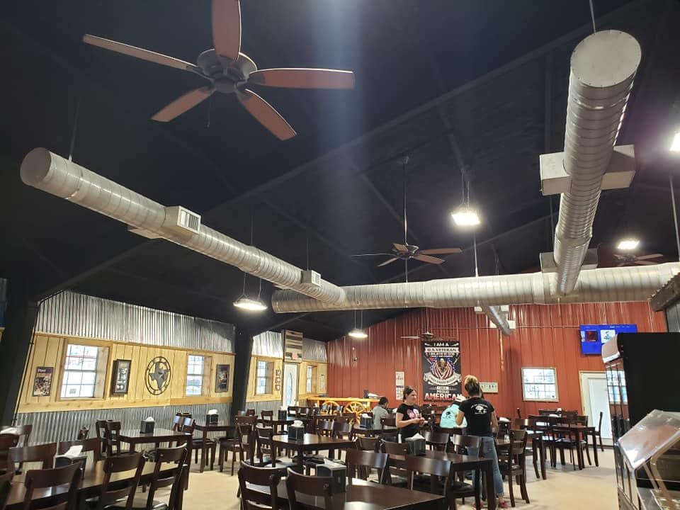 Indoor dining area with dark wooden tables, chairs, exposed ductwork on a black ceiling, and walls with rustic wood siding.
