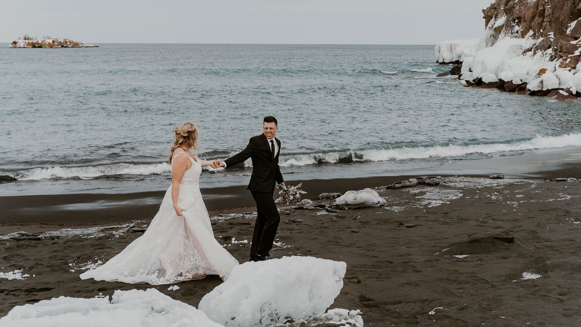 A bride and groom are walking on a snowy beach.