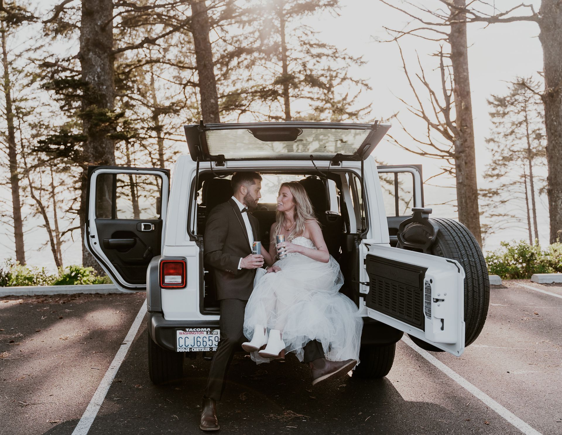 A bride and groom are sitting in the back of a white jeep.