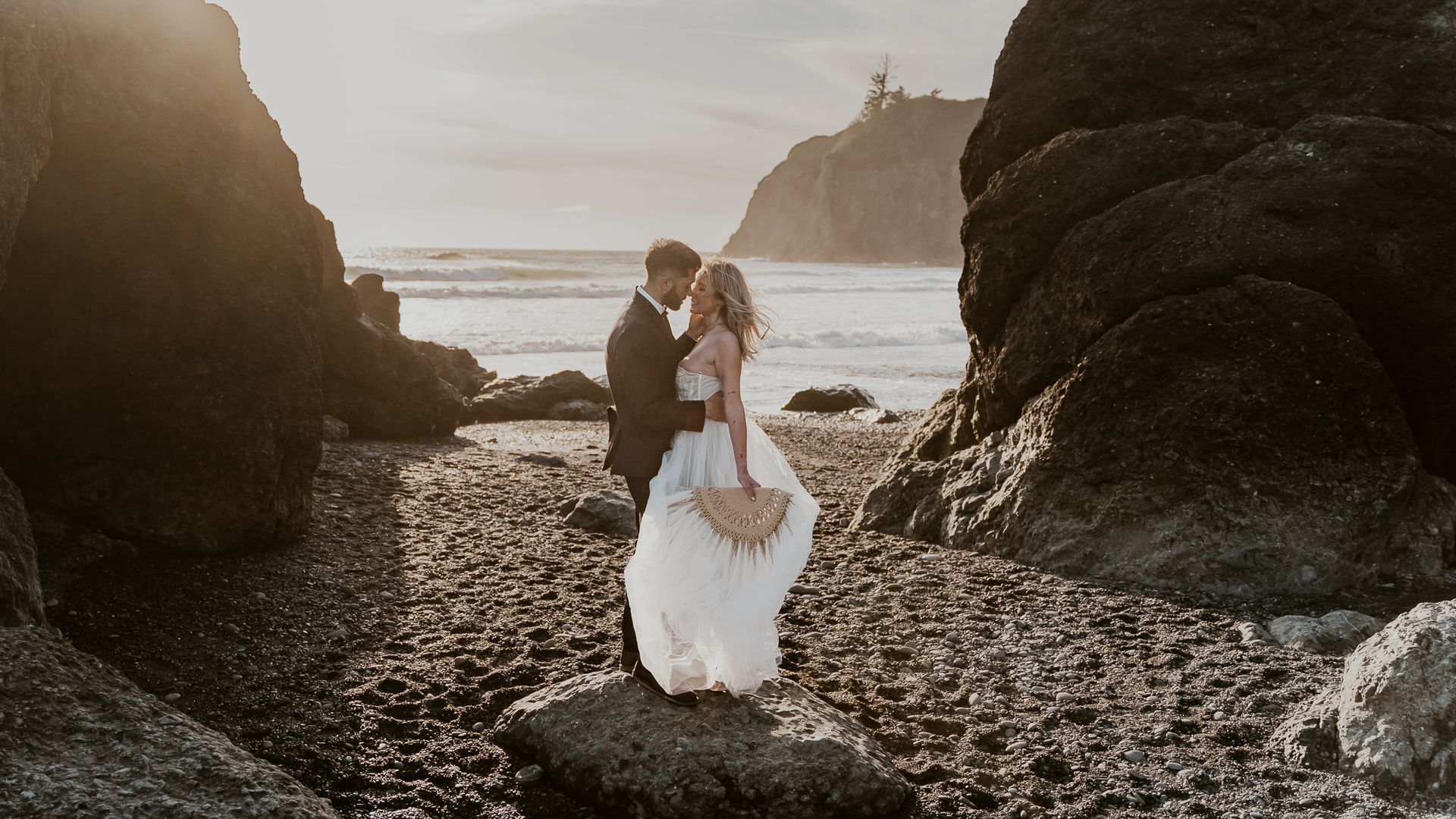 A bride and groom are standing on a rocky beach.