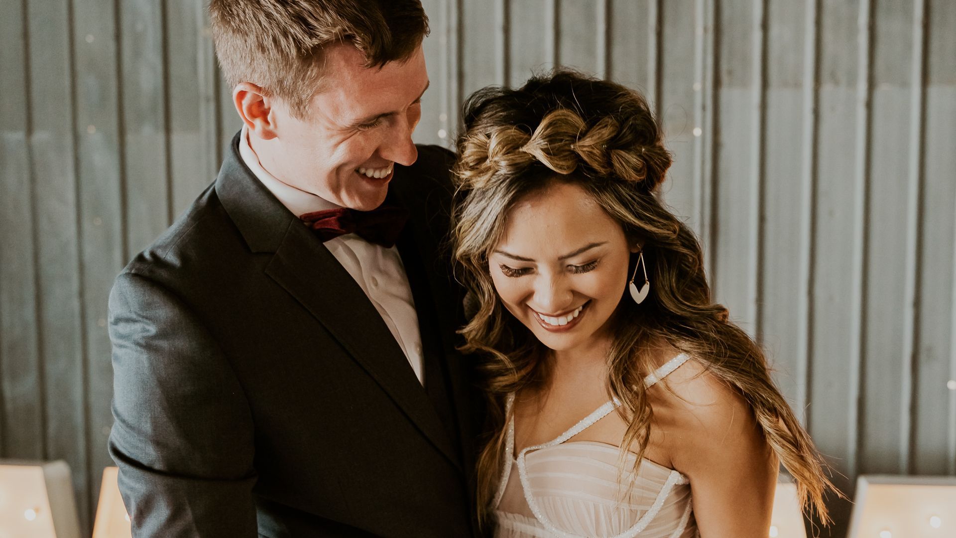 A bride and groom are standing next to each other and smiling at their wedding cake.