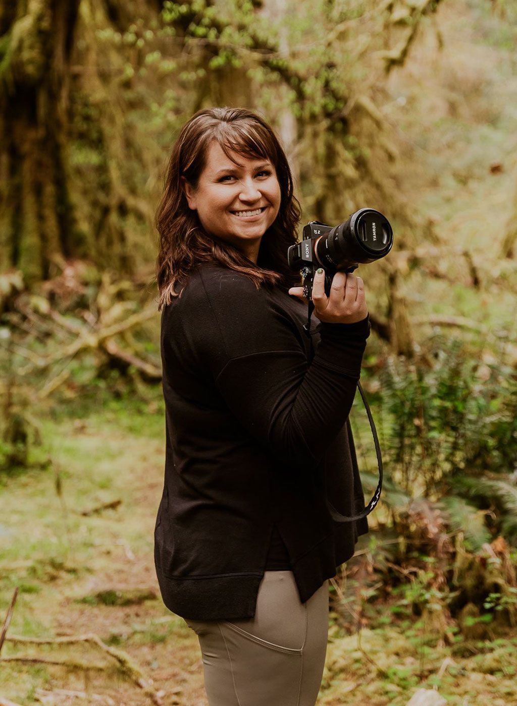 A woman is holding a camera in a forest.
