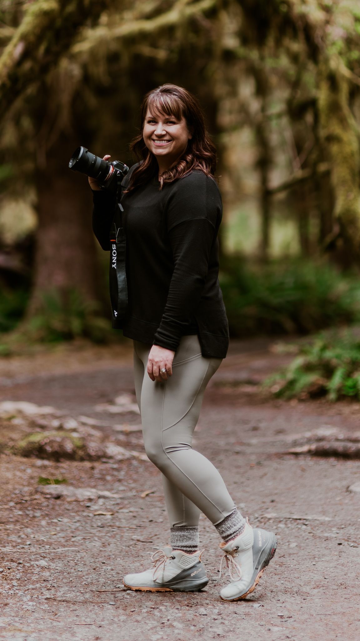 a woman is walking down a path in the woods holding a camera .