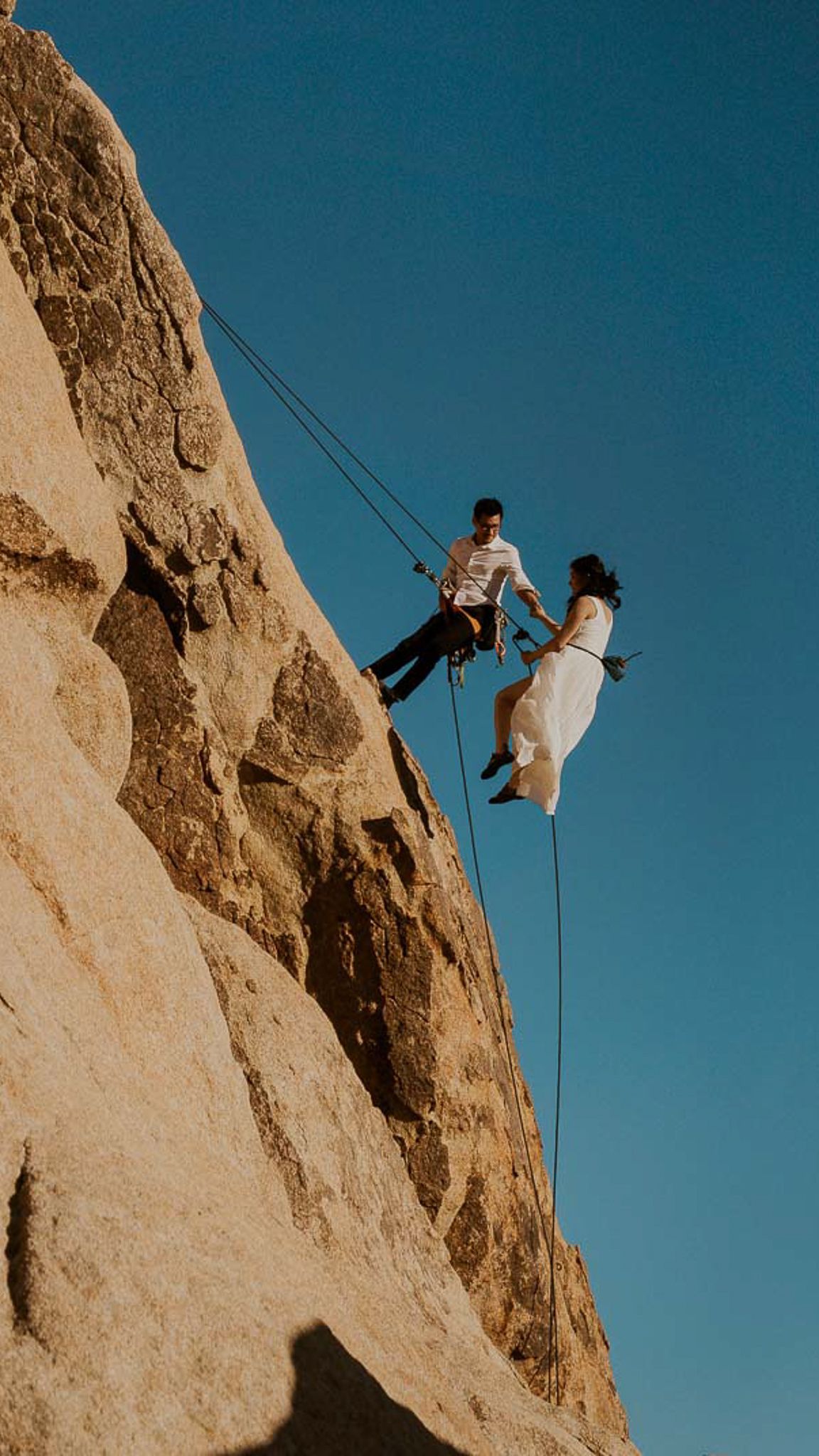 a man and a woman are climbing up the side of a mountain .