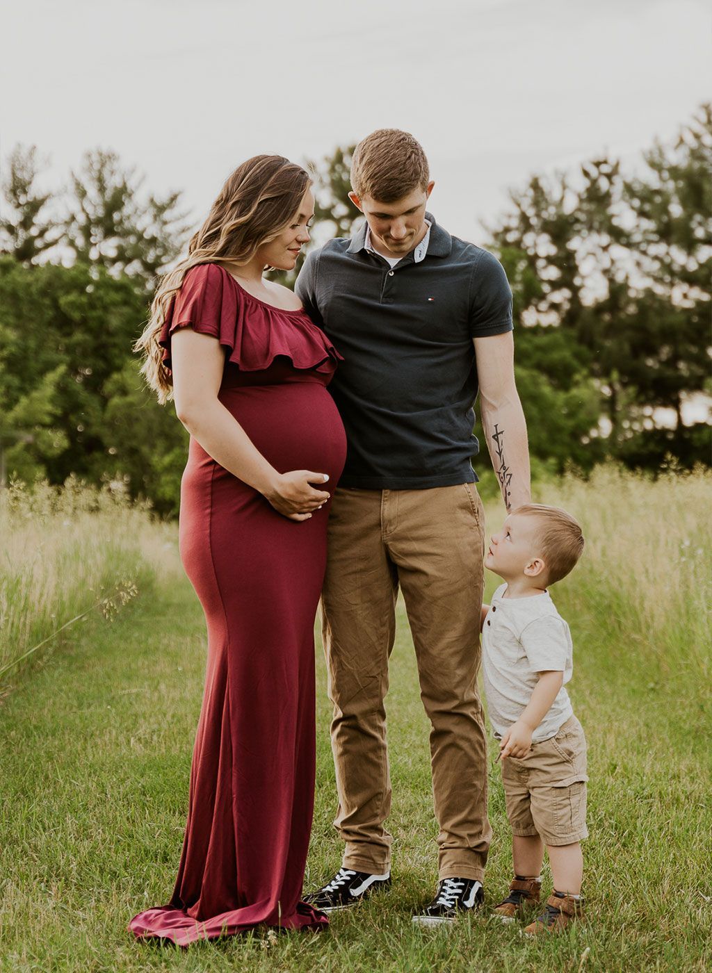a pregnant woman is standing next to a man and a little boy in a field .