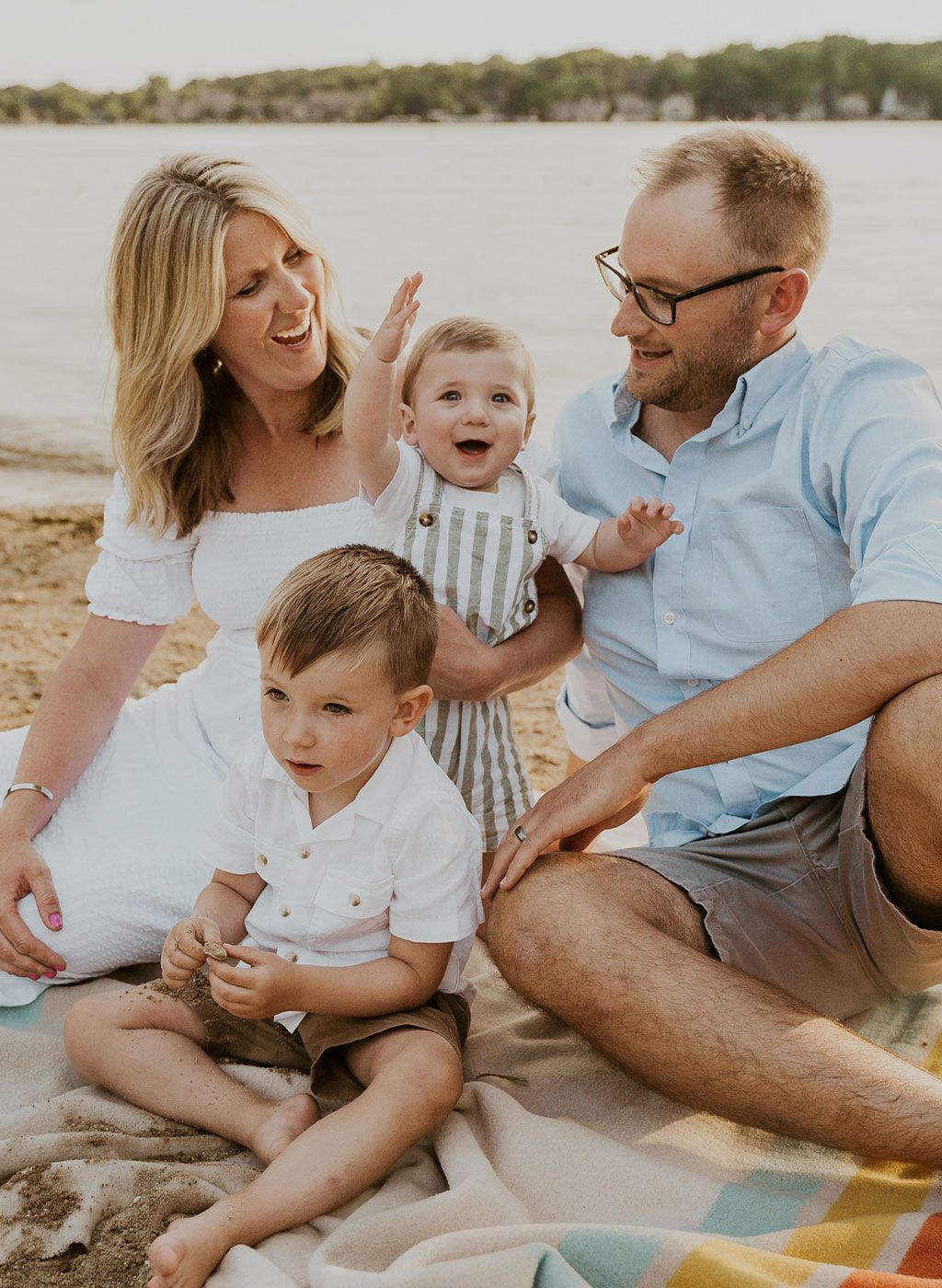 a family is sitting on a blanket on the beach .