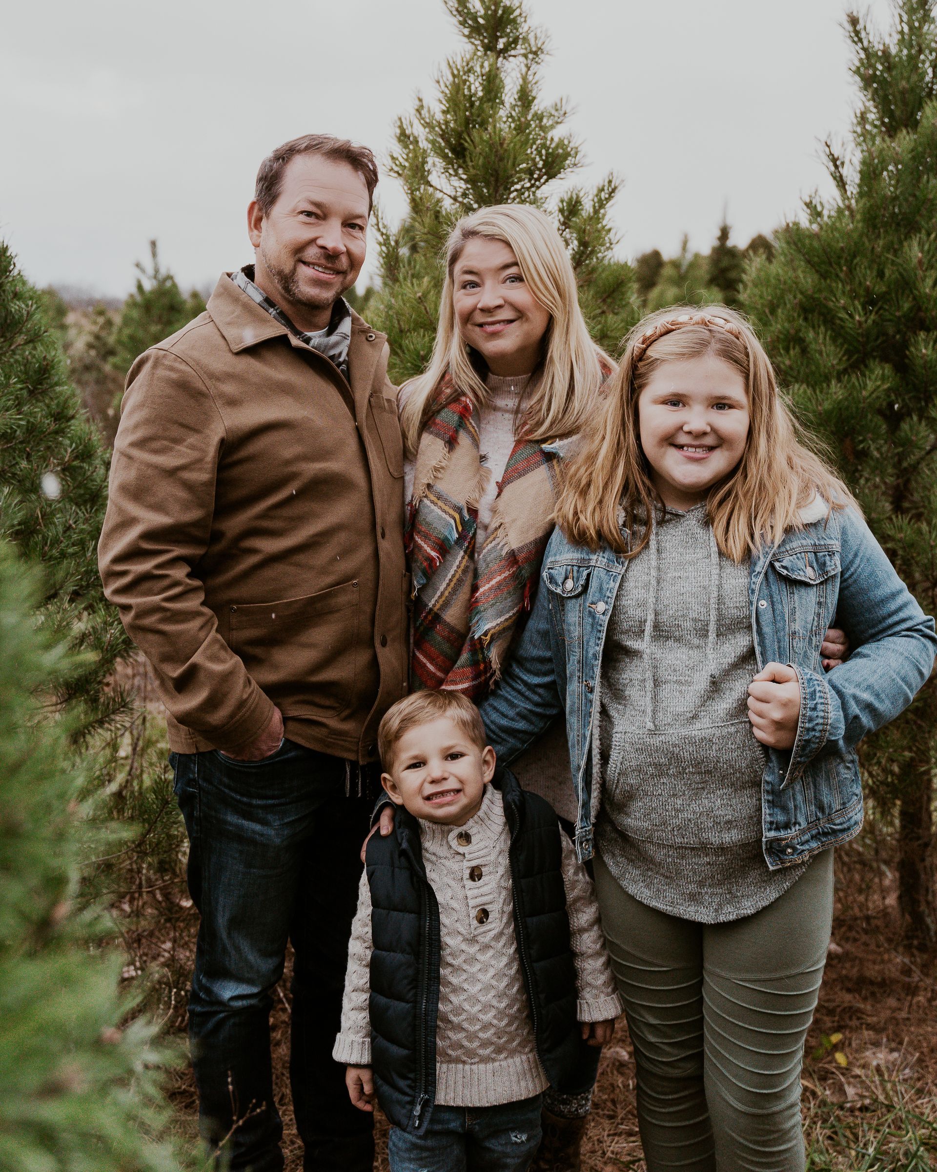 A family is posing for a picture in a christmas tree farm.