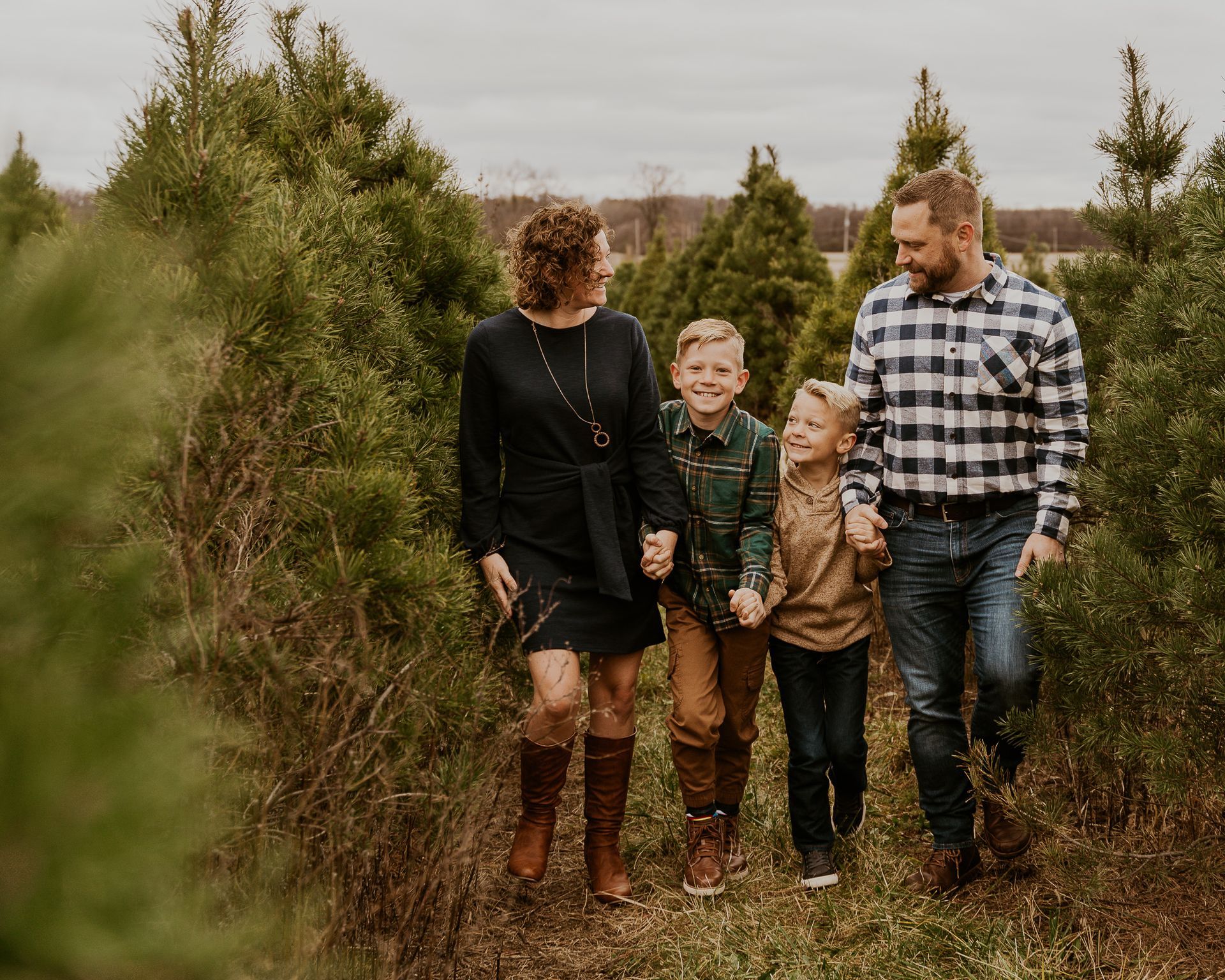 A family is walking through a christmas tree farm holding hands.