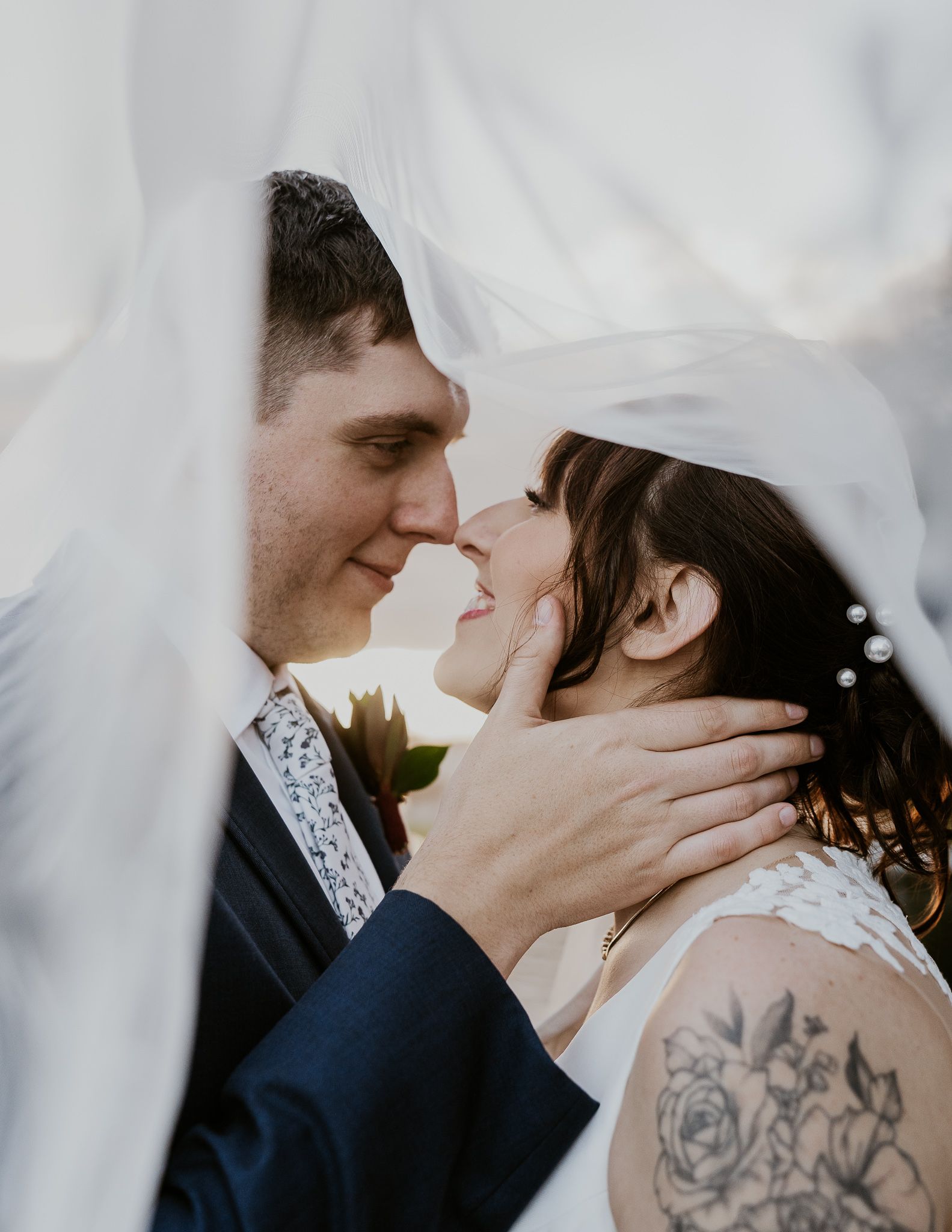 A bride and groom are standing next to each other in front of a window holding a bouquet of flowers.