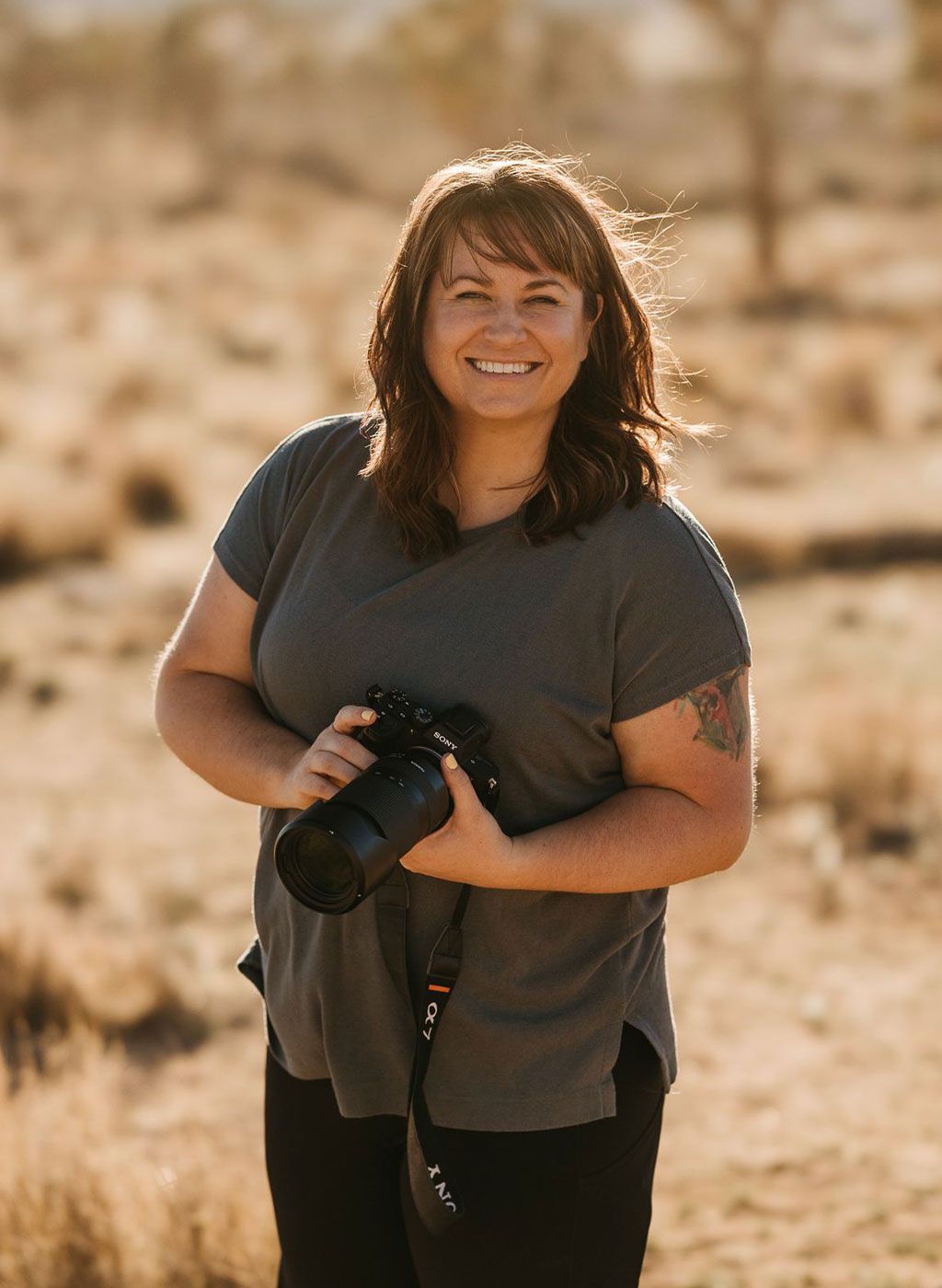 a woman is holding a camera in a field and smiling .