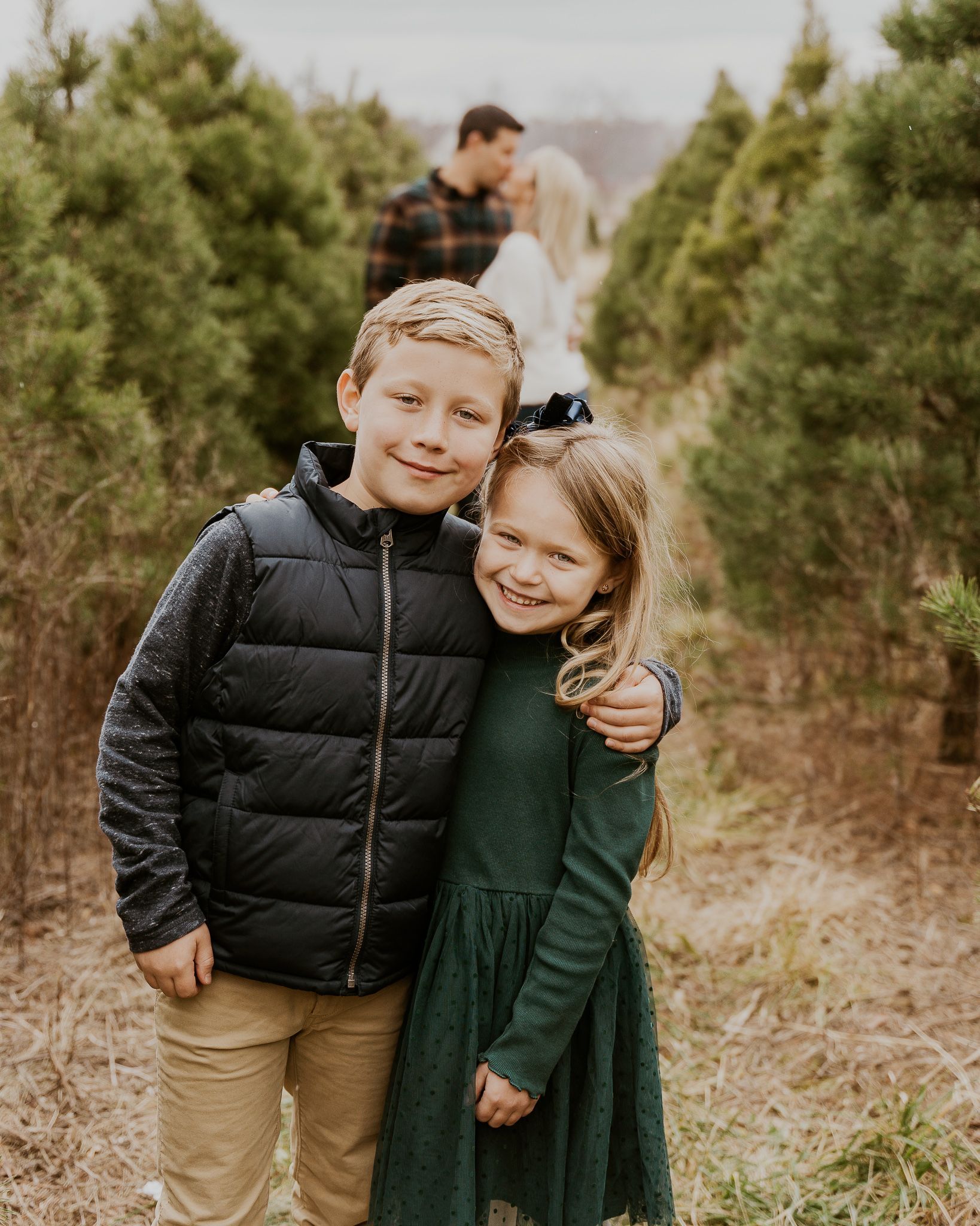 A boy and a girl are posing for a picture in a christmas tree farm.