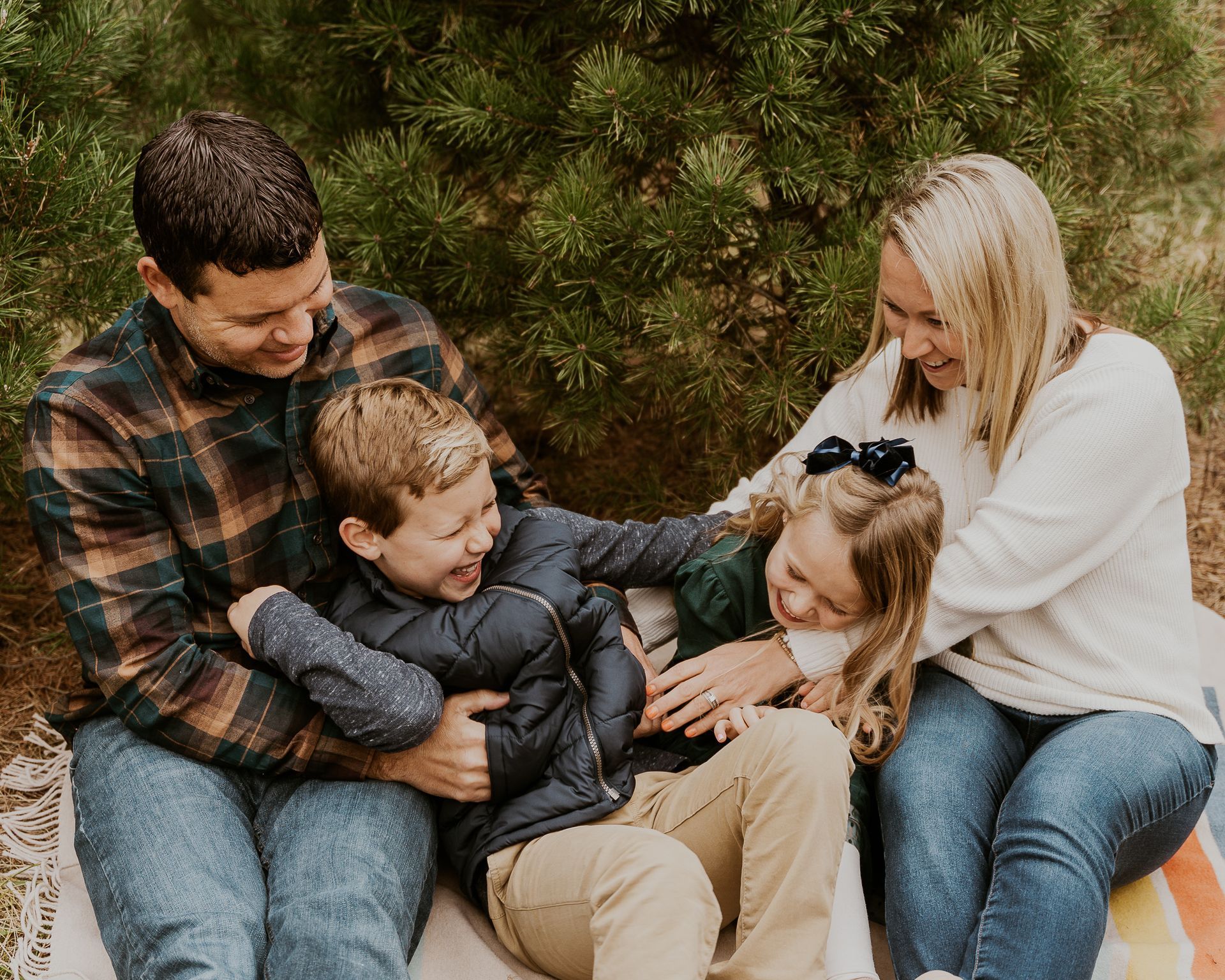 A family is sitting on a blanket in front of a christmas tree.