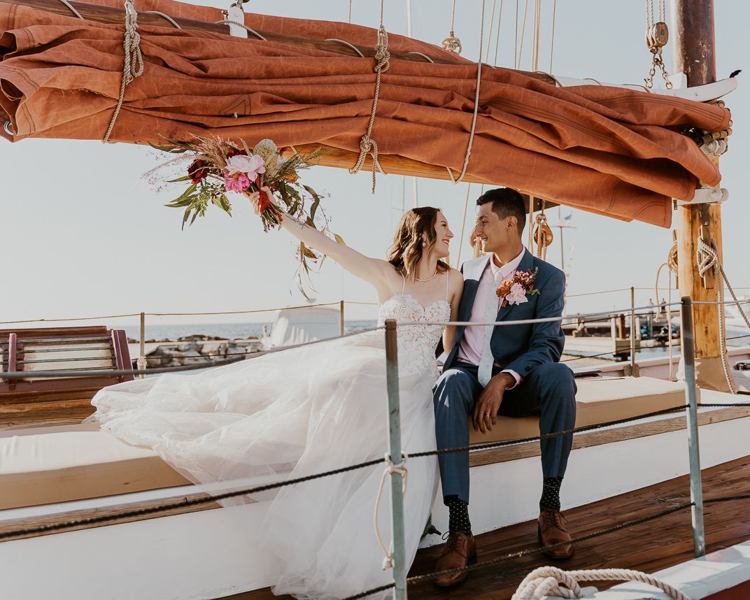 A bride and groom are sitting on the deck of a sailboat.