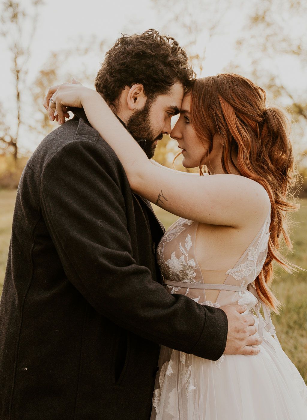 a bride and groom are hugging and looking at each other in a field .
