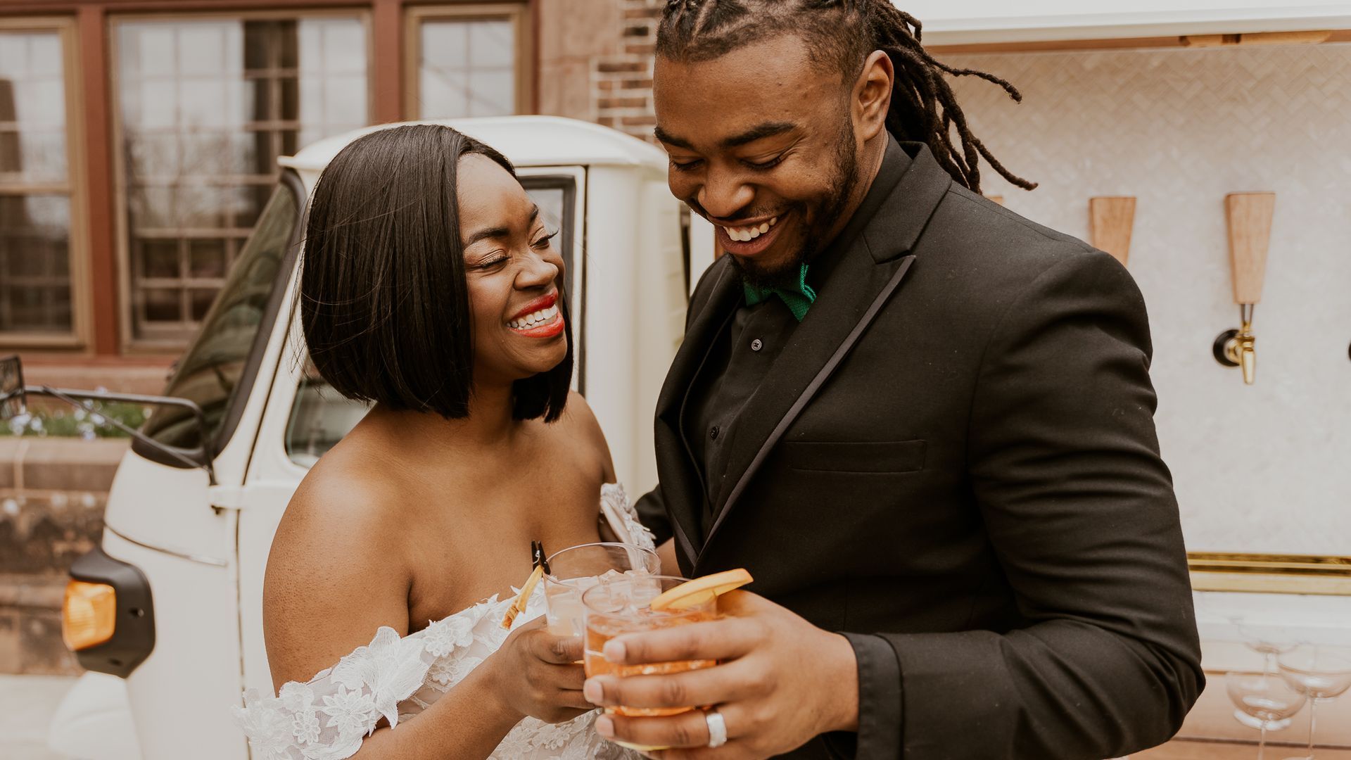 a bride and groom are toasting with drinks in front of a truck .
