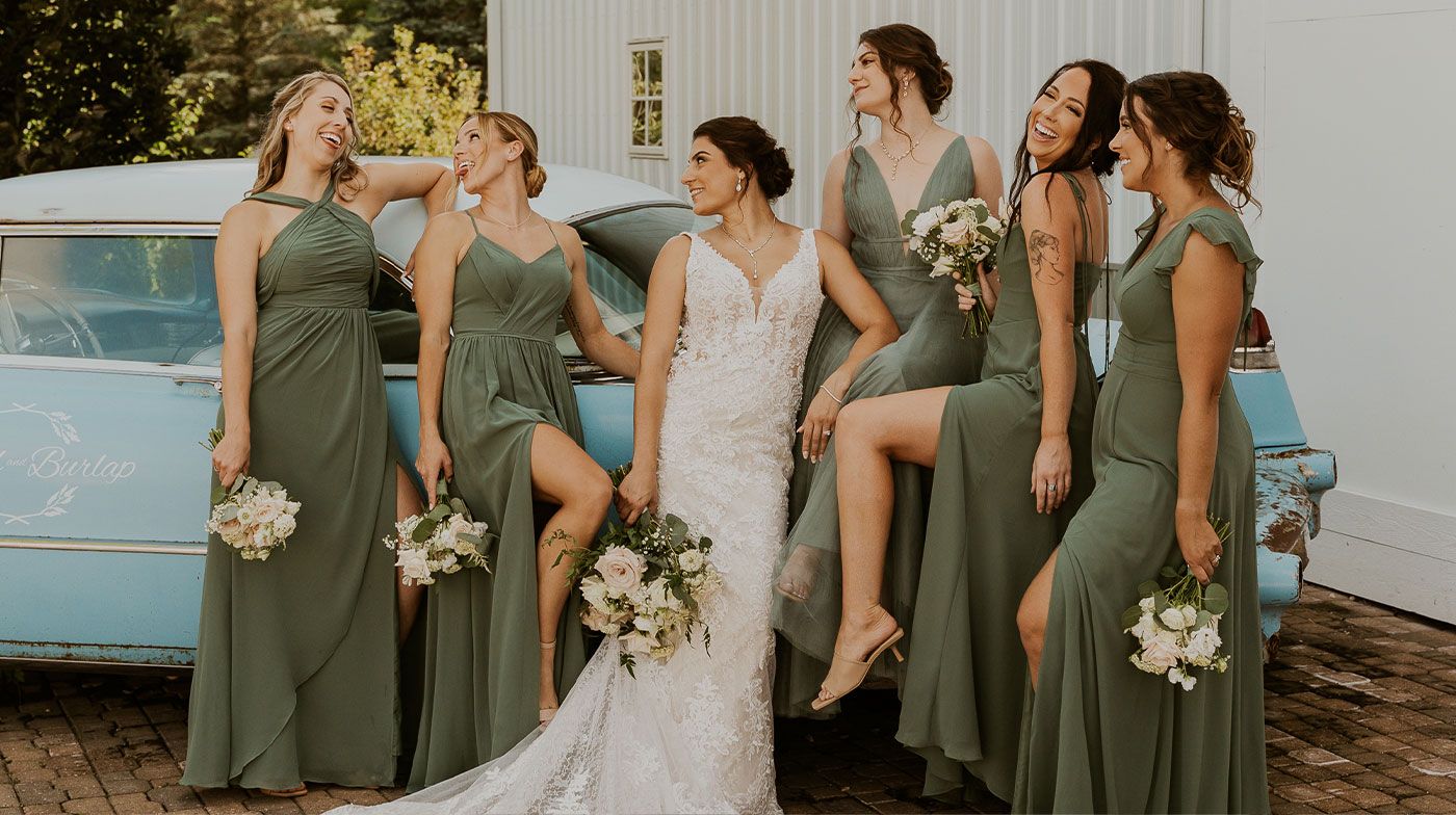 A bride and her bridesmaids are posing for a picture in front of a car.