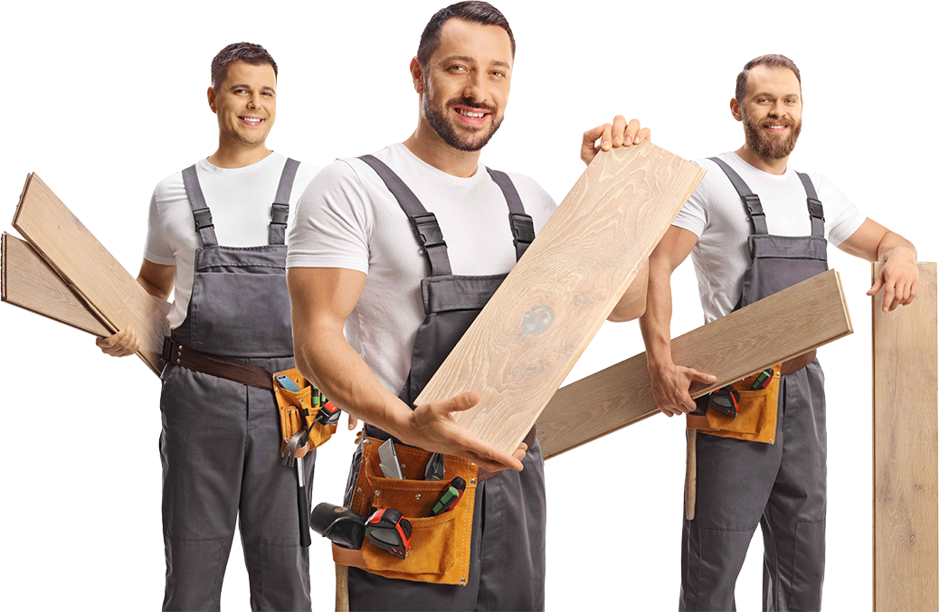 Three workers holding wooden planks, smiling, wearing gray overalls and white shirts.
