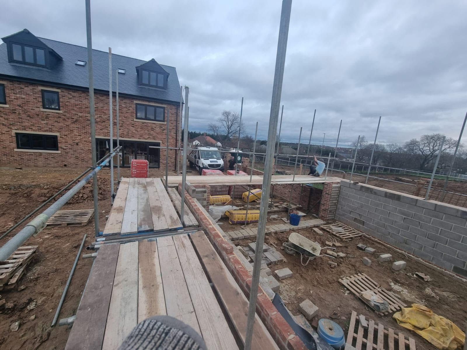 Construction site with a brick house and scaffolding, cloudy sky.