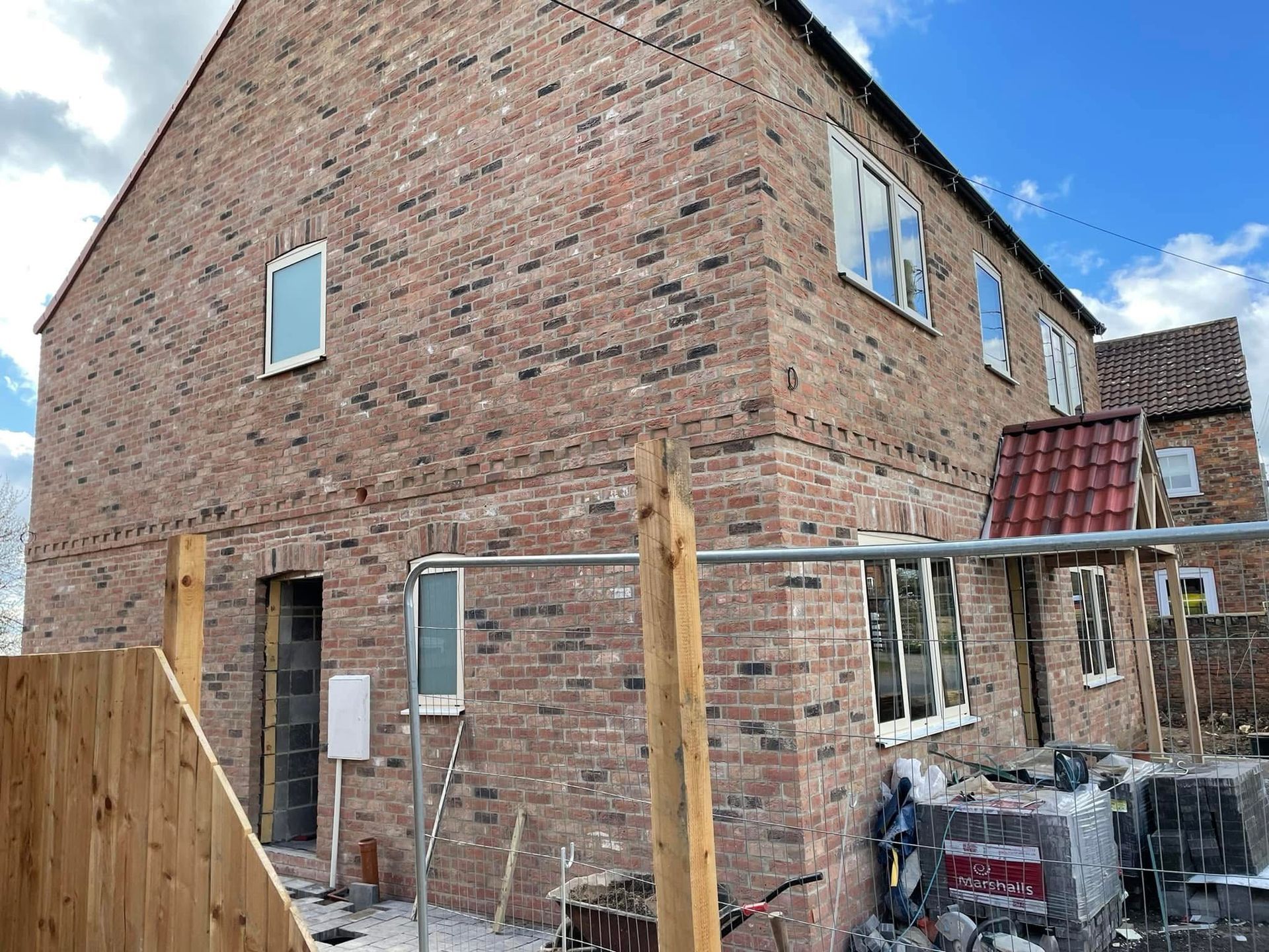 Brick house under construction with multiple windows and wooden fencing.