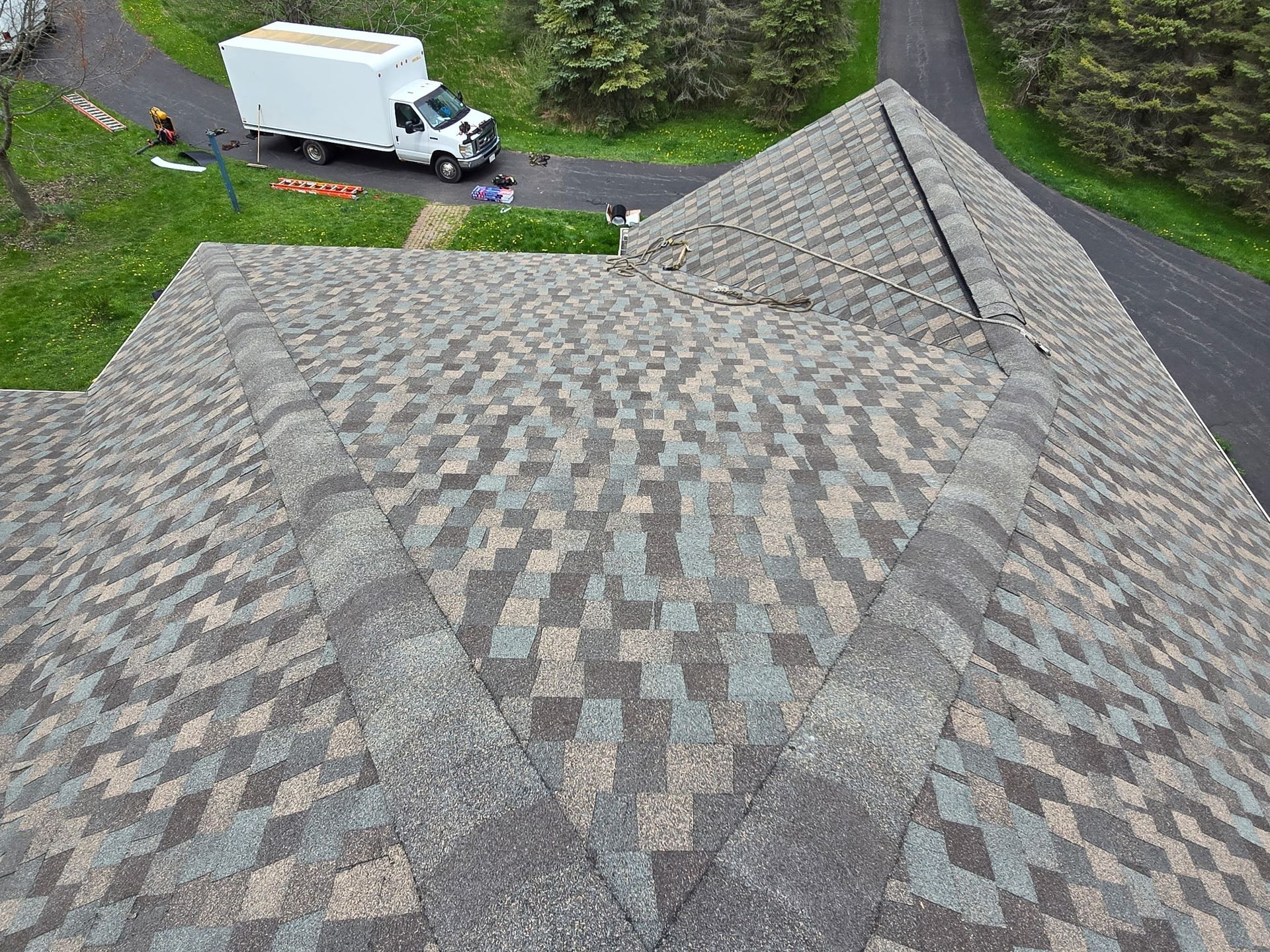 An overhead view of a gray shingled roof with a white truck parked on a driveway below.