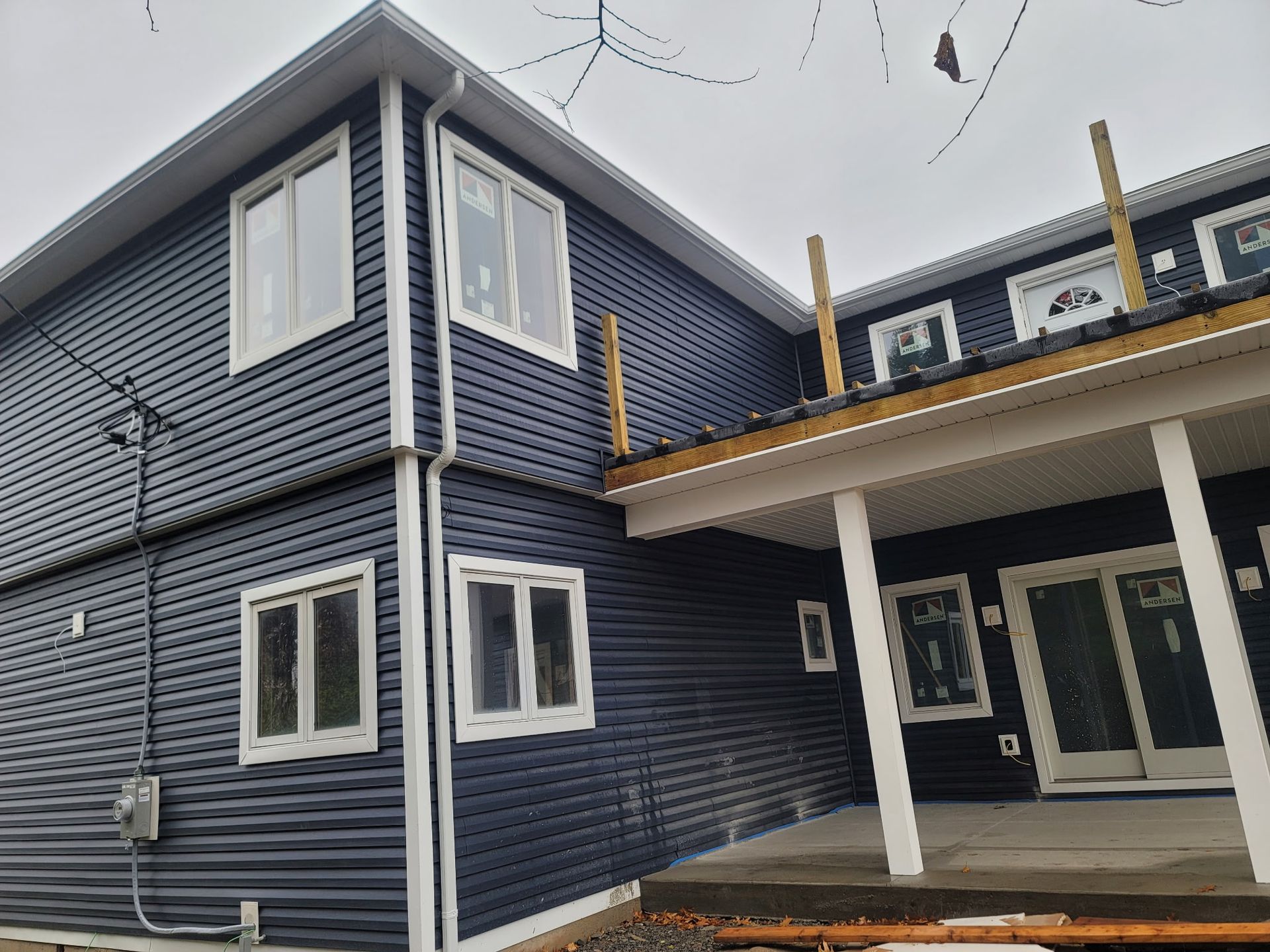 A two-story house with dark blue horizontal siding, white window trim, and a partially constructed wooden deck.