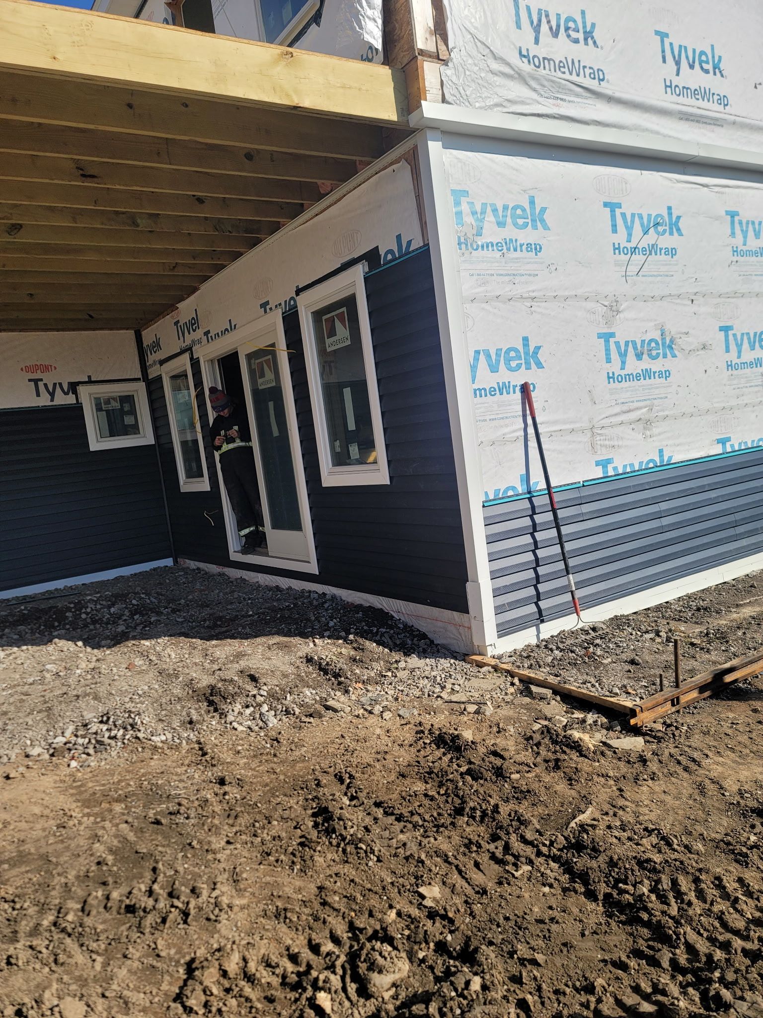 Construction site showing a house with blue siding, white window trim, and Tyvek house wrap on an unfinished wall.