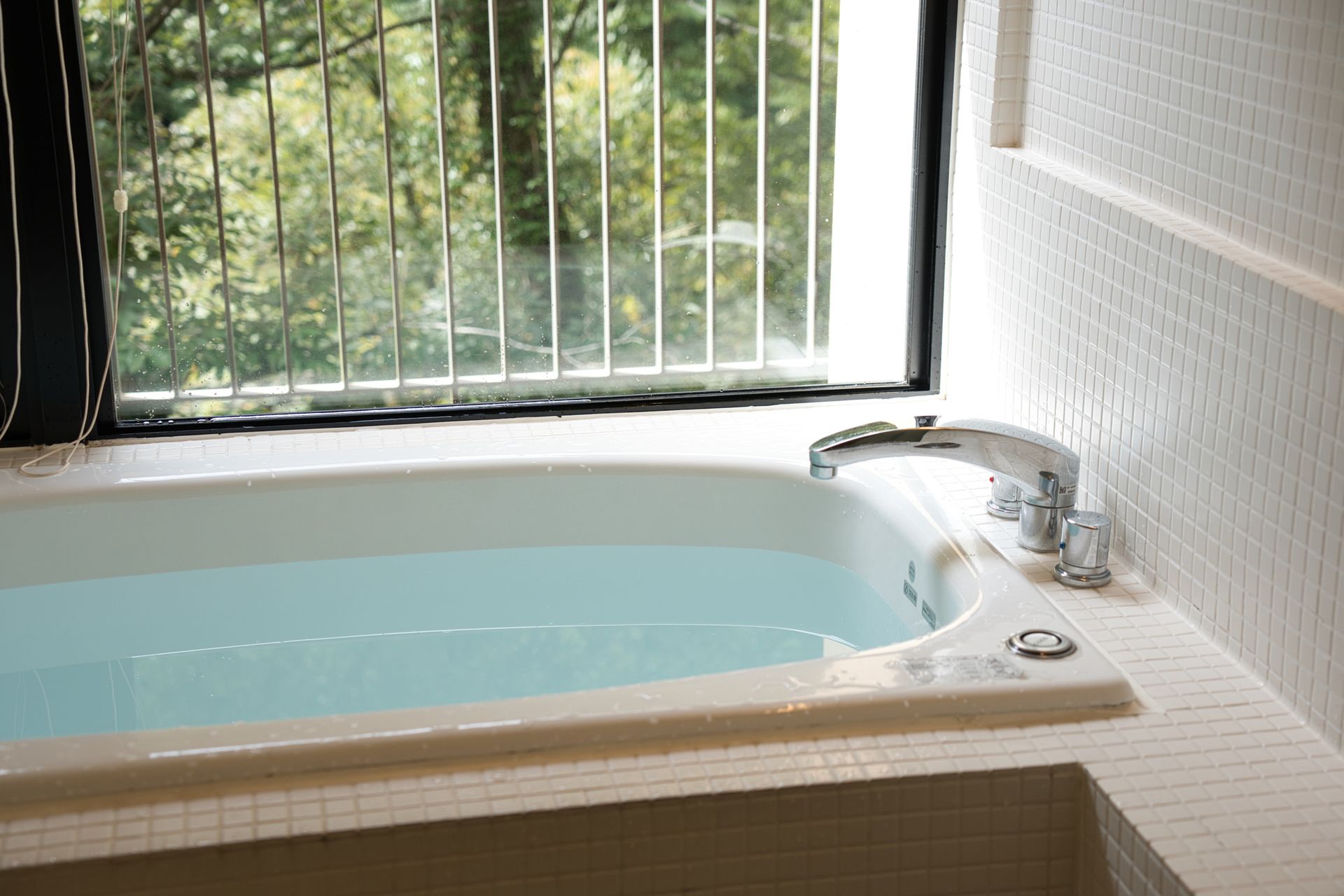 A bathtub filled with water in a bathroom next to a window.