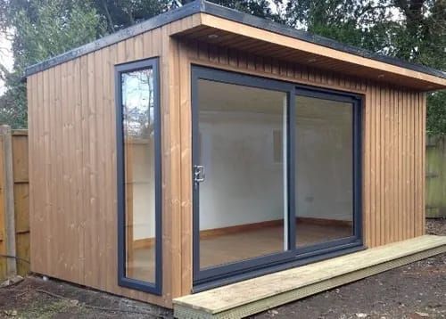 Oficina de jardín de madera con grandes puertas corredizas de vidrio y ventana lateral.