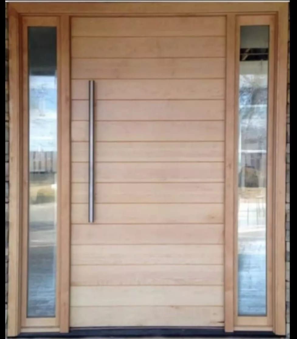 Puerta de madera con tirador metálico vertical, flanqueada por dos ventanas altas y estrechas.
