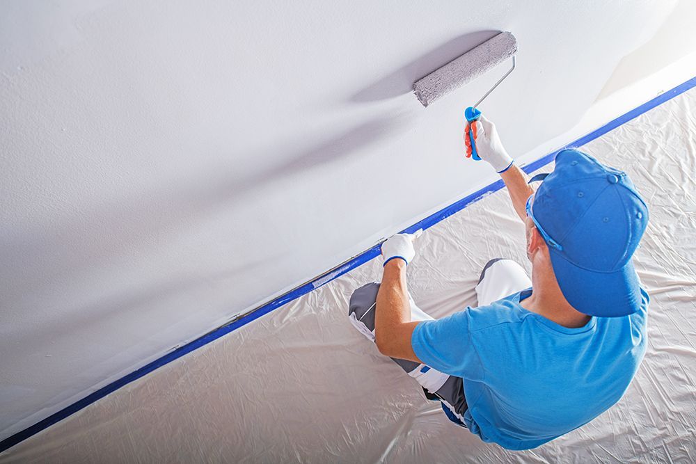 A man is sitting on the floor painting a wall with a roller.