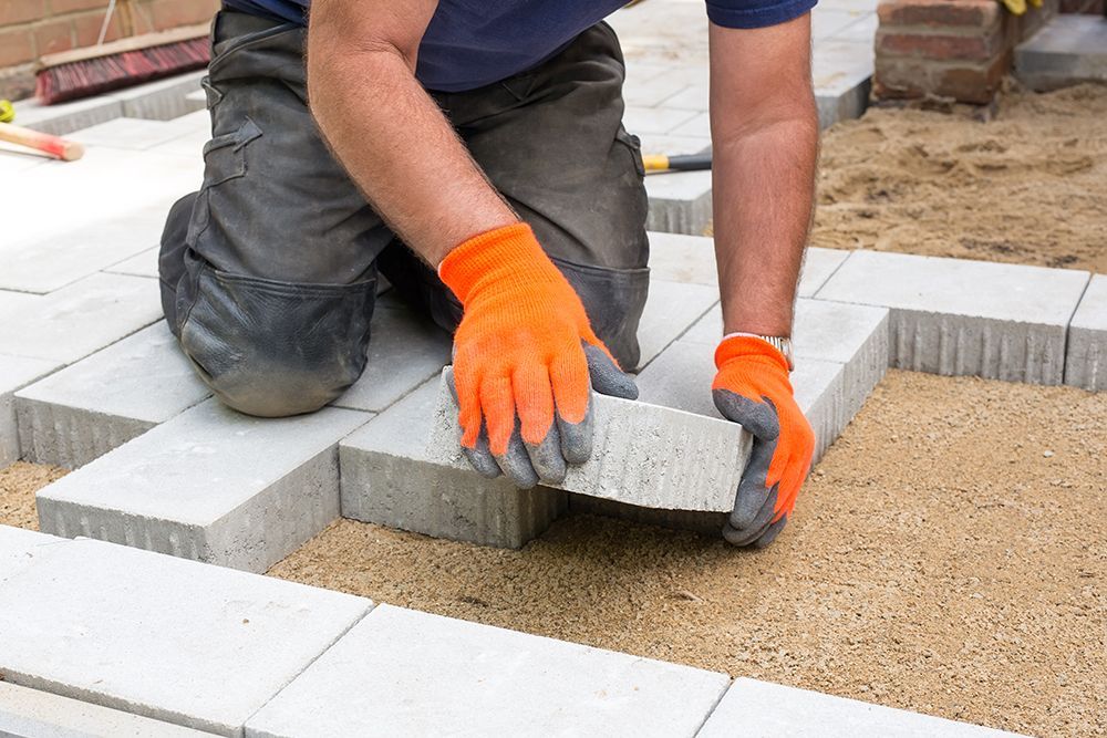 A man wearing orange gloves is laying bricks on a sidewalk.
