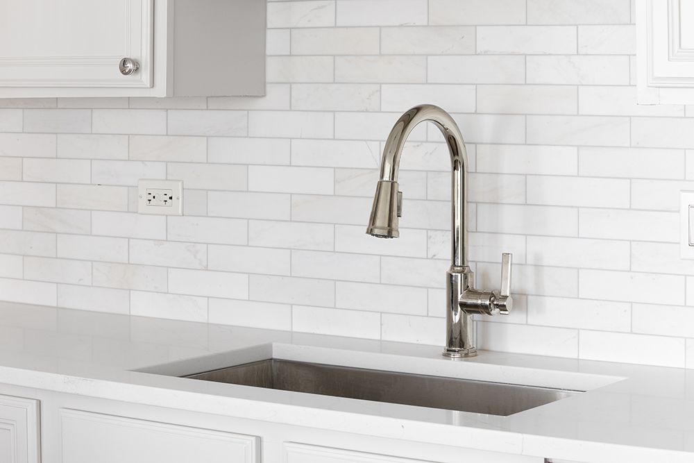 A kitchen sink with a faucet and white tiles on the wall.