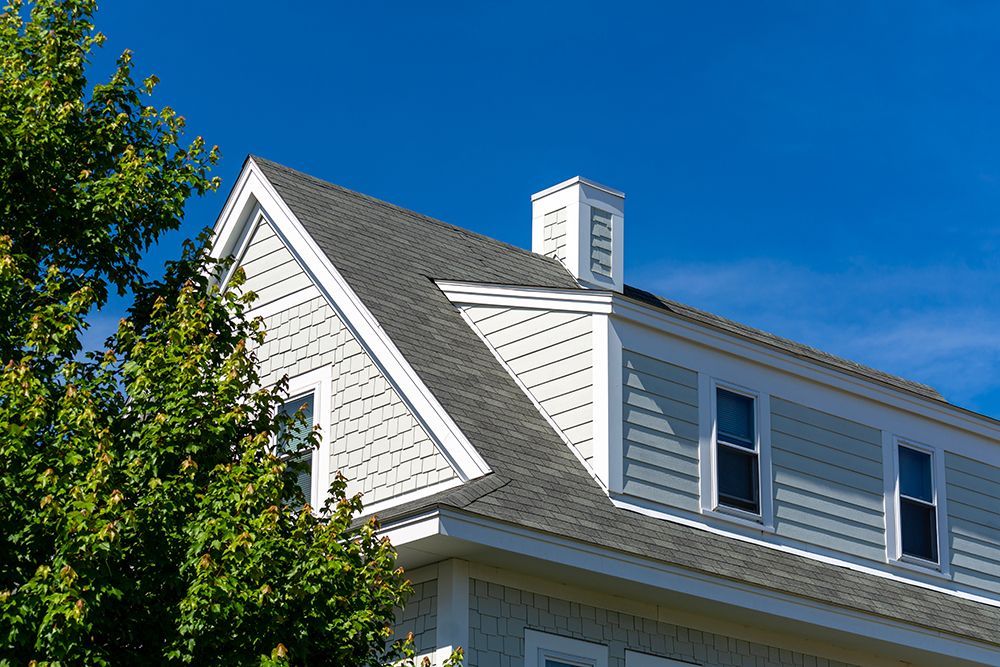 A house with a chimney on the roof and a tree in front of it.